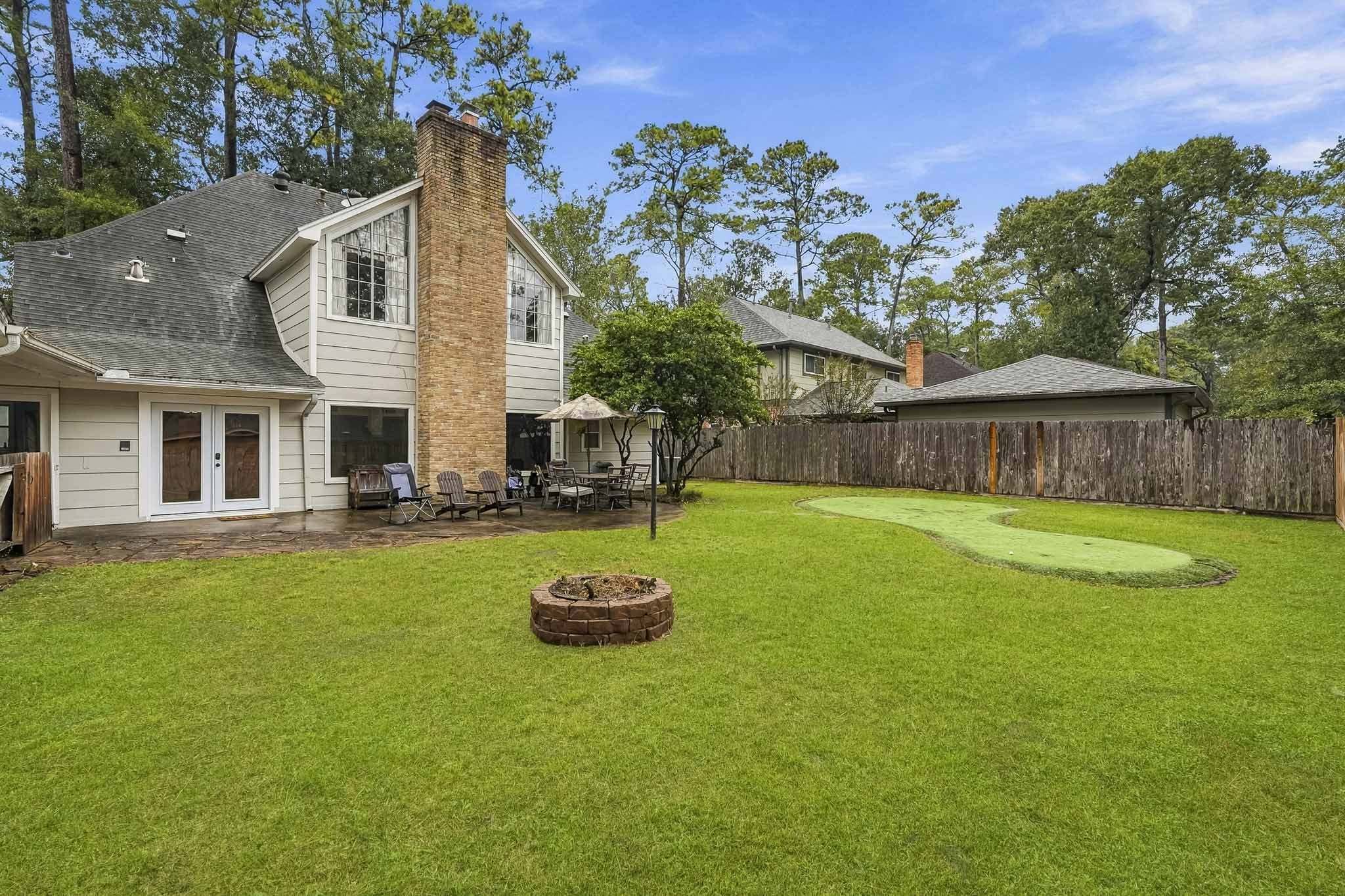 Beautiful backyard featuring a spacious lawn, cozy fire pit, and patio area perfect for outdoor gatherings, all set against a backdrop of mature trees.