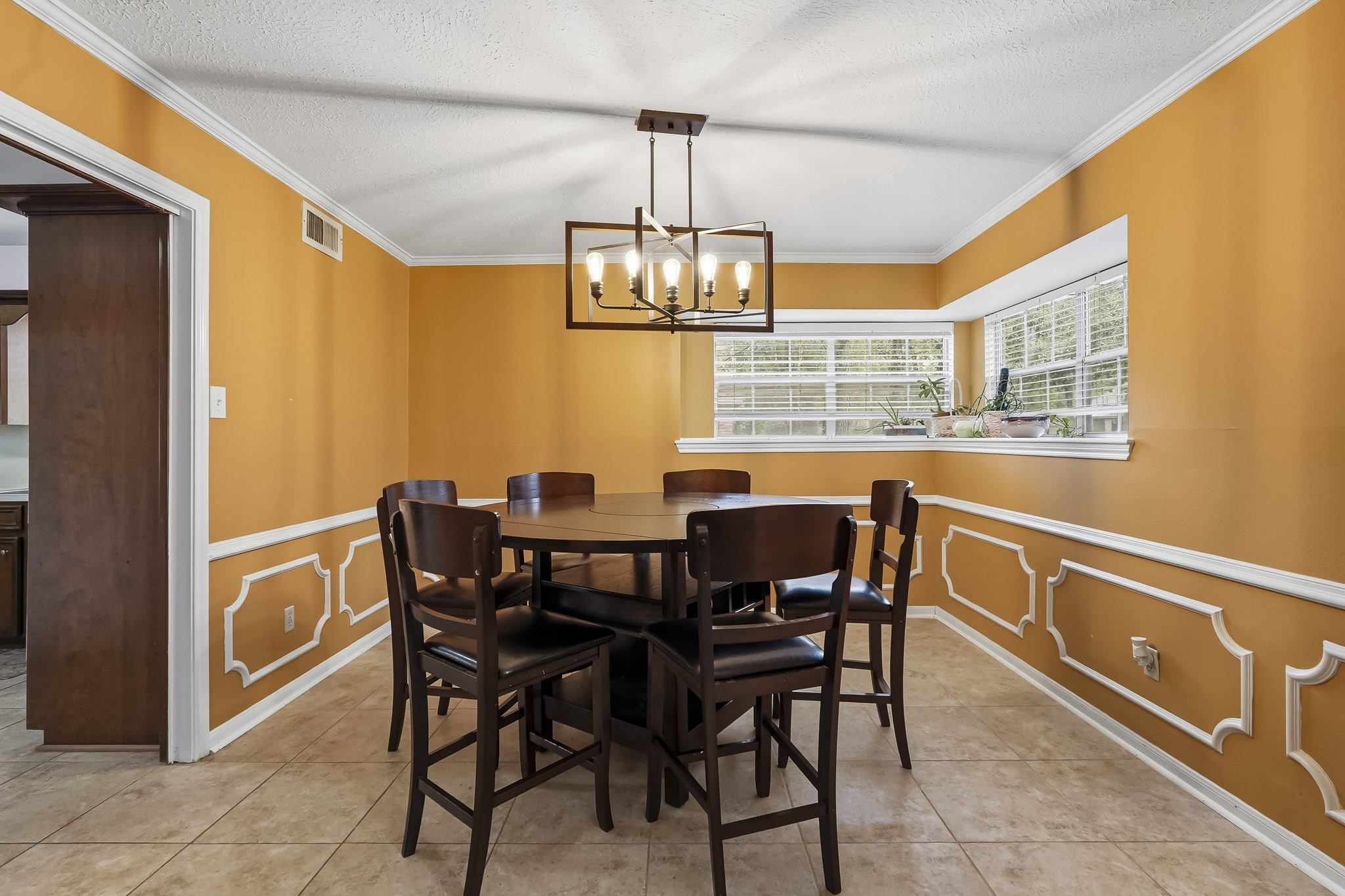 Bright dining area with elegant wainscoting, and a stylish chandelier, offering ample natural light through large corner windows.