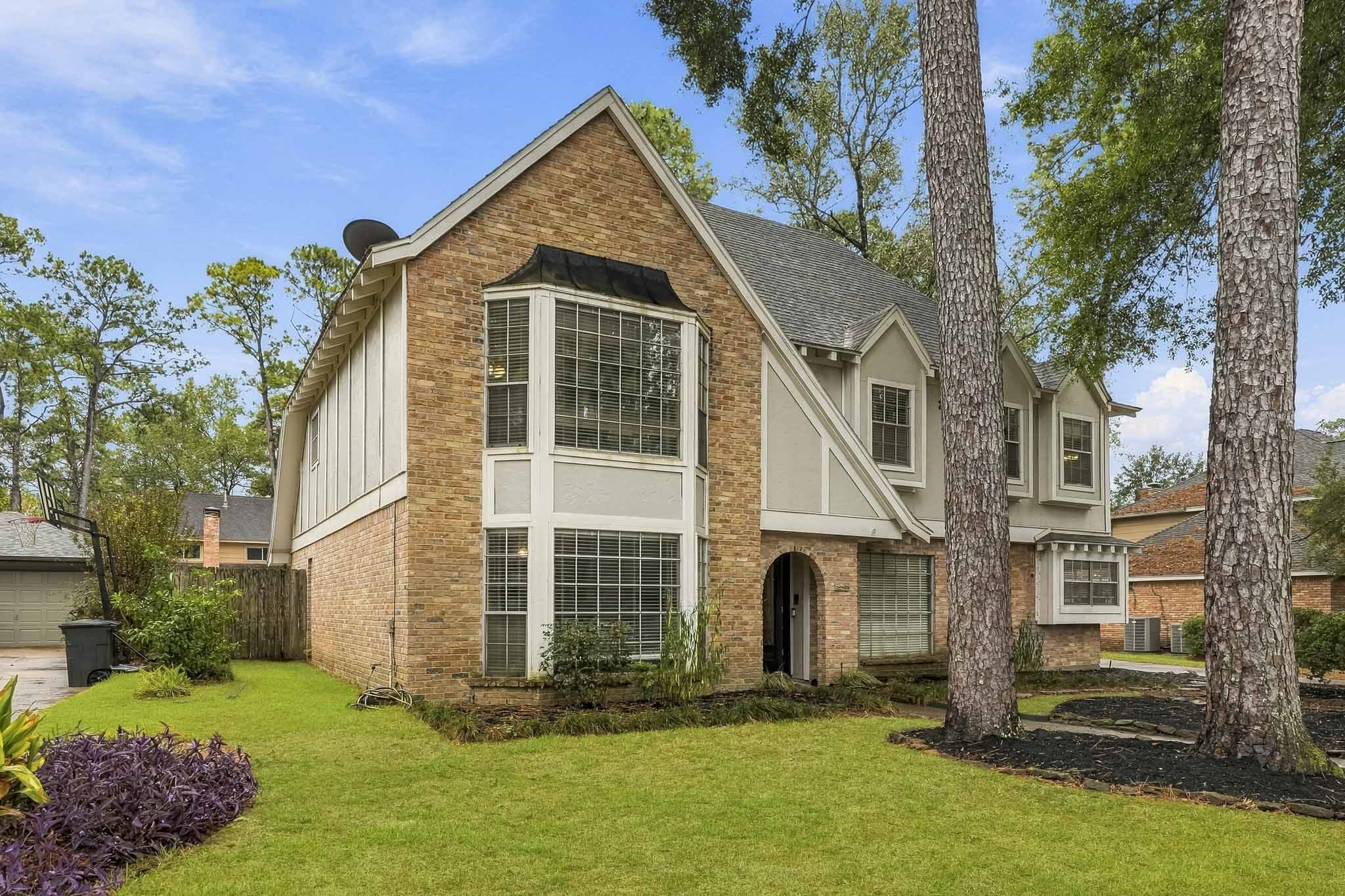 Charming two-story brick home with large bay windows, nestled among mature trees, offering a spacious front lawn and inviting curb appeal.