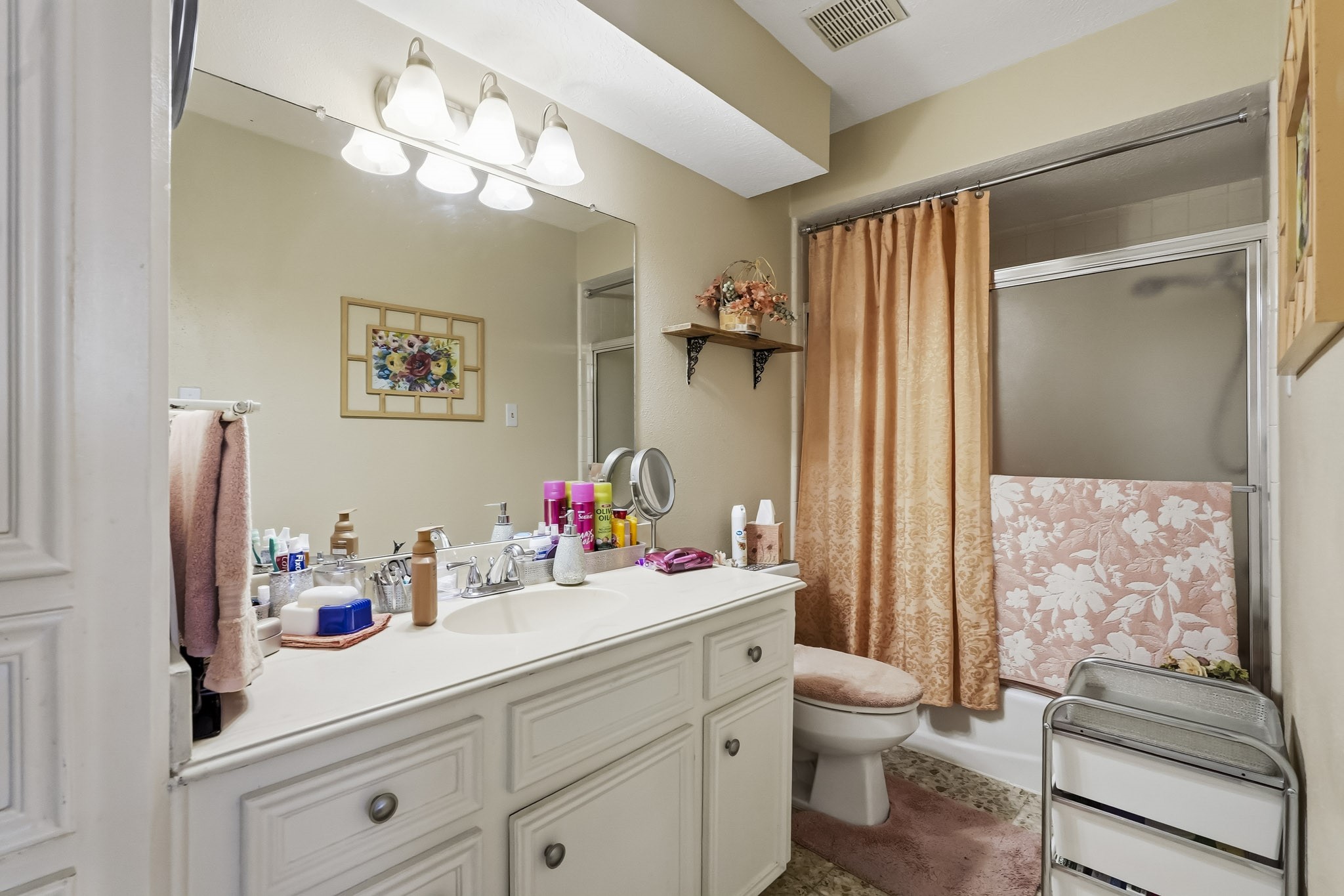 Charming secondary bathroom featuring a spacious vanity with ample storage, elegant lighting, and a tub-shower combination.