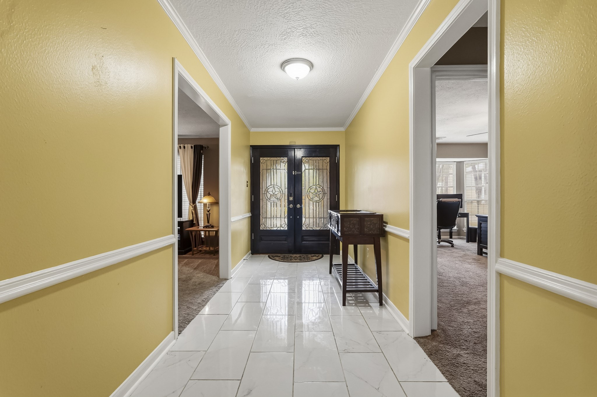 Bright and welcoming entryway featuring elegant tile flooring and a stylish black front door with decorative glass panels.