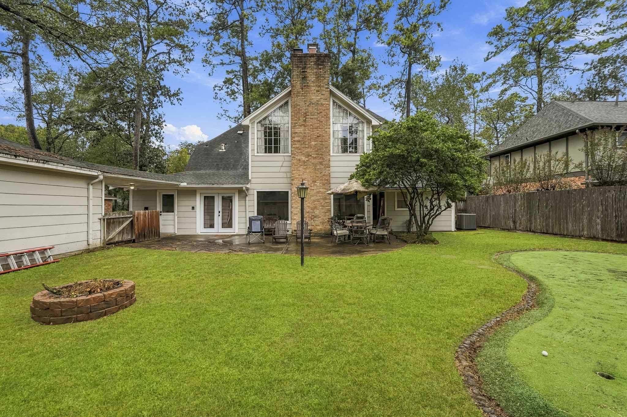 Charming backyard retreat featuring a spacious patio, lush greenery, a cozy fire pit, and a putting green, perfect for outdoor entertaining and relaxation.