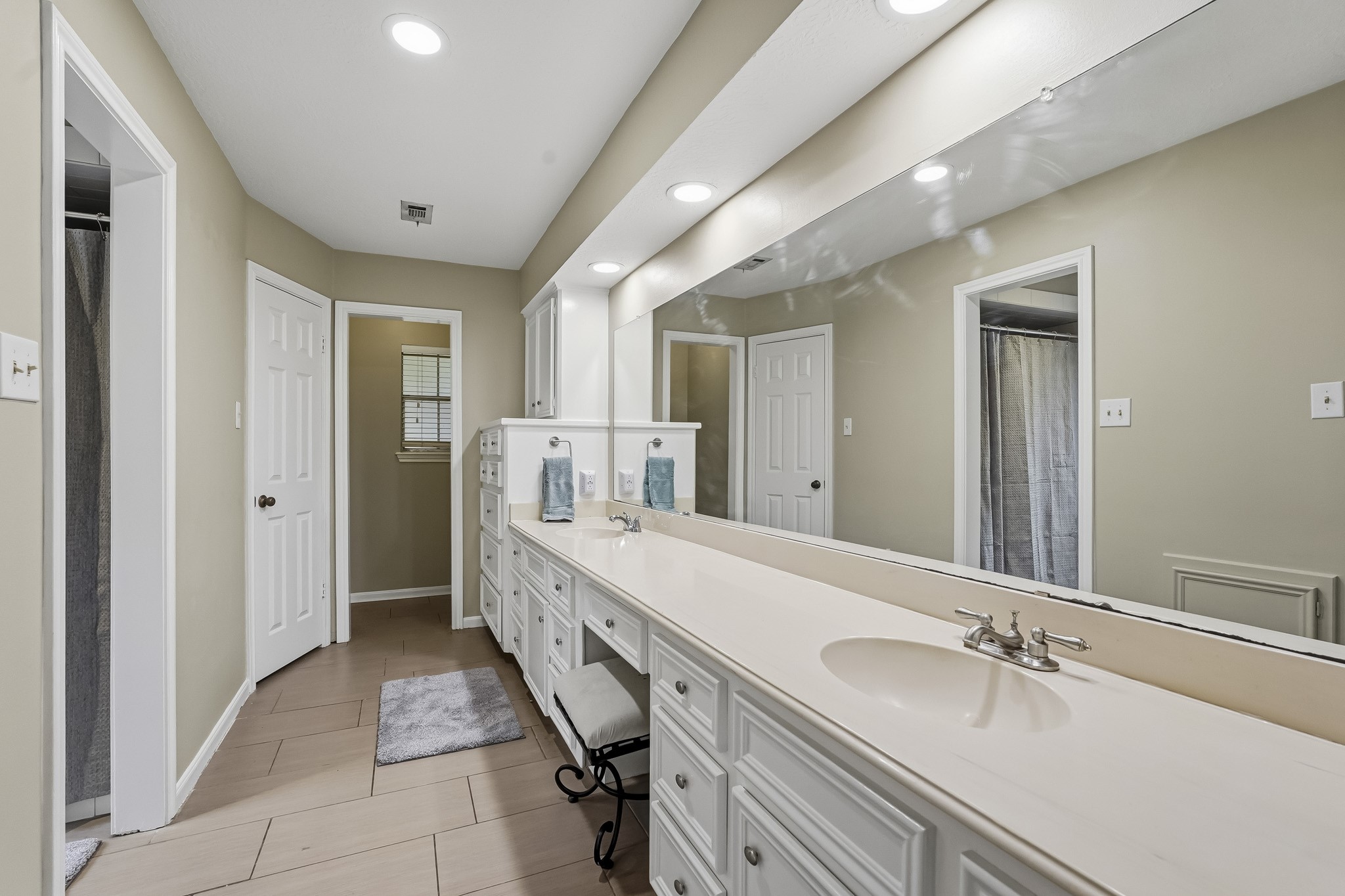 Spacious primary bathroom featuring a long vanity with dual sinks, ample cabinetry, a large mirror, and modern lighting.