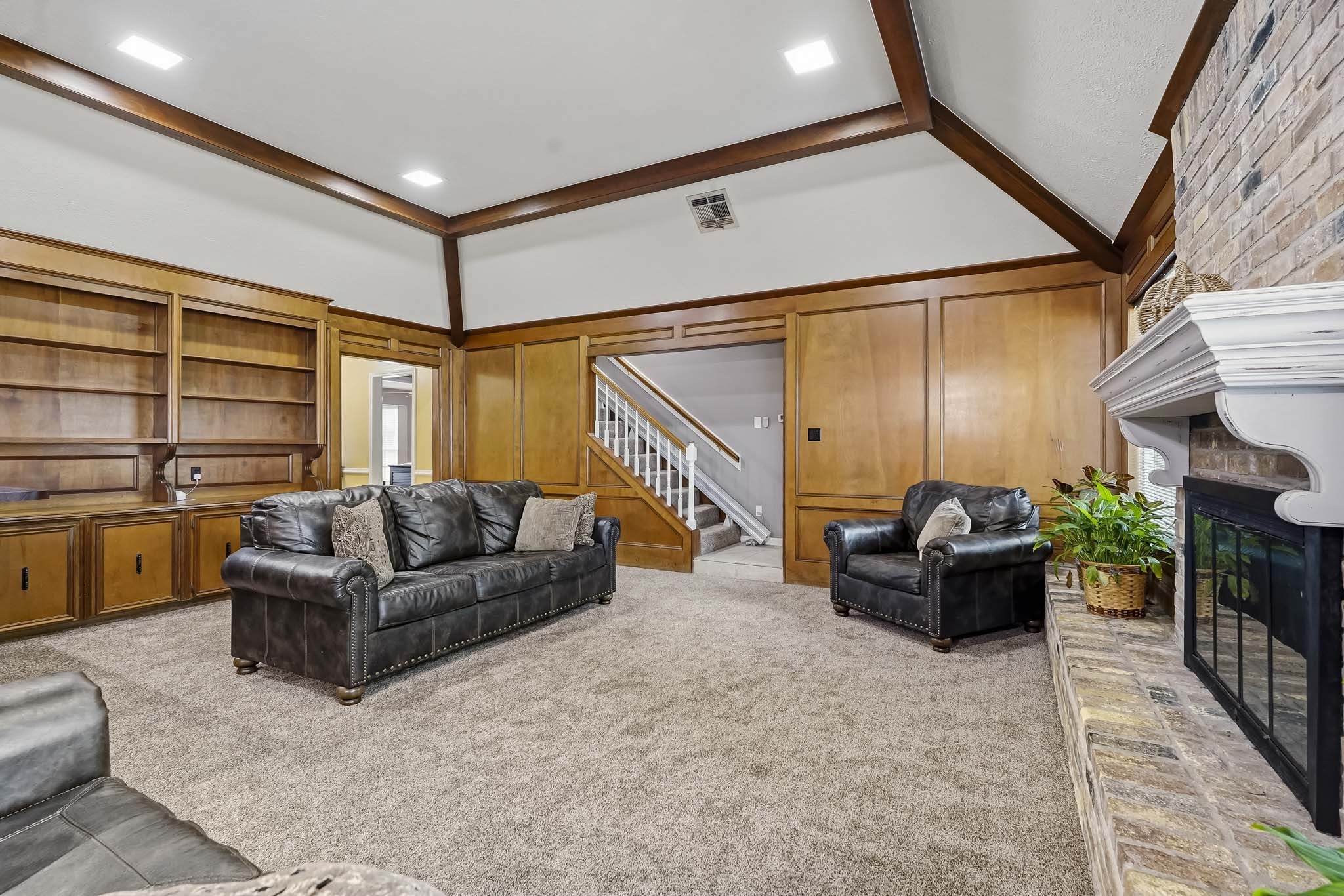 Spacious living room featuring elegant wood paneling, a cozy fireplace with a brick surround, built-in shelving.