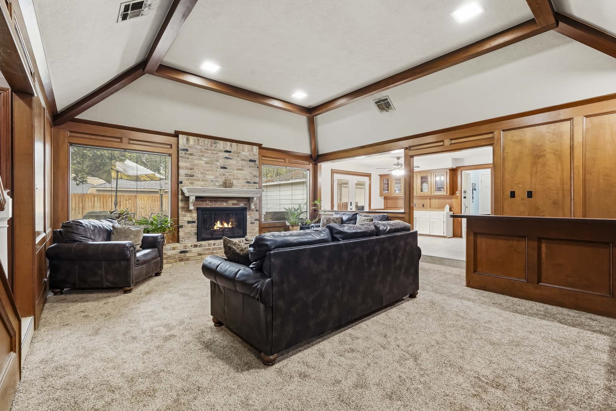 Spacious living room with vaulted ceilings, featuring a cozy brick fireplace and large windows that invite natural light.