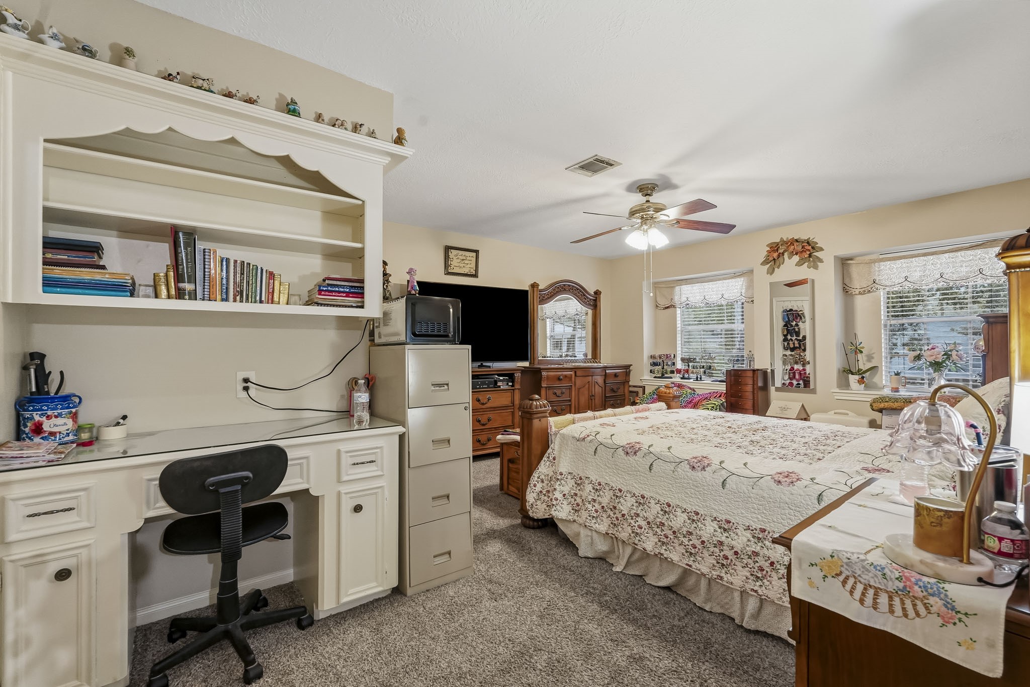 Spacious secondary bedroom with cozy carpet features a built-in desk, ample shelving, and large windows for natural light, complemented by a ceiling fan.