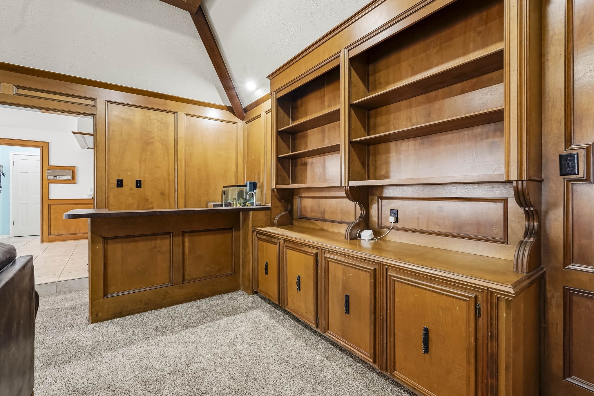 Elegant wooden built-in bookshelves offer ample storage and display space, seamlessly blending with the rich wood paneling and cozy carpeted flooring, creating a warm, inviting atmosphere.