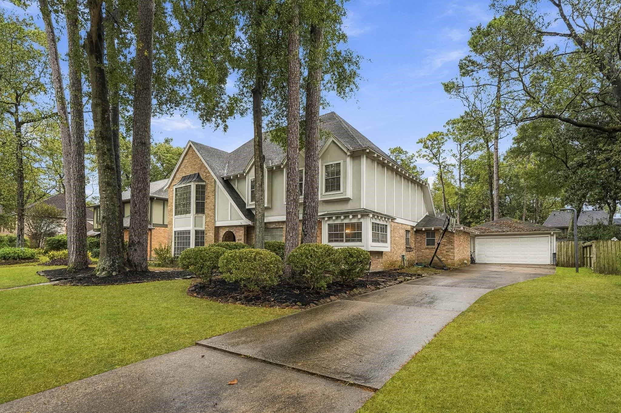 Charming two-story home nestled among mature trees, featuring a classic brick and siding exterior with a spacious driveway leading to a detached garage.