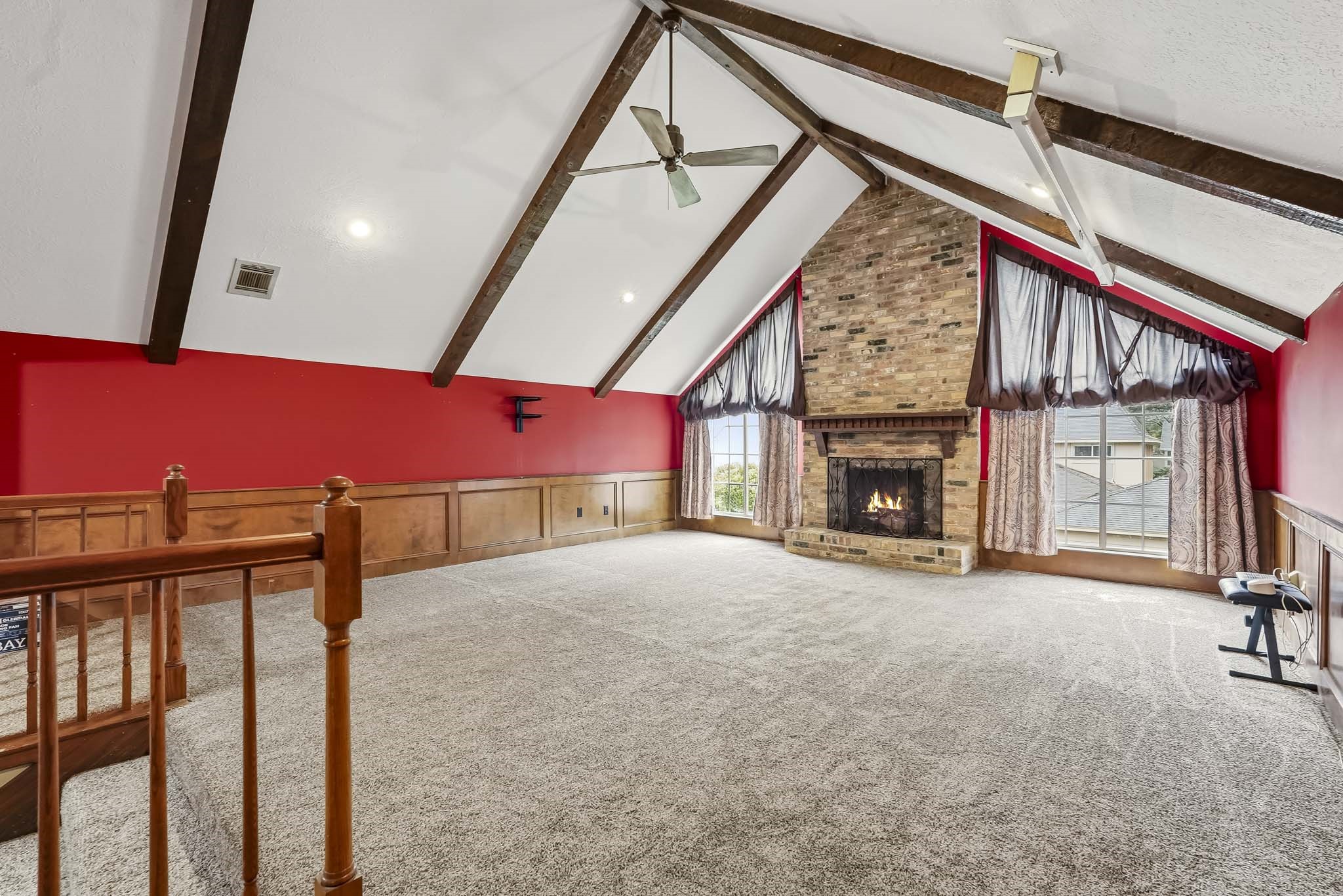 Expansive game room with vaulted ceilings, exposed beams, and a striking brick fireplace, complemented by large windows for natural light.