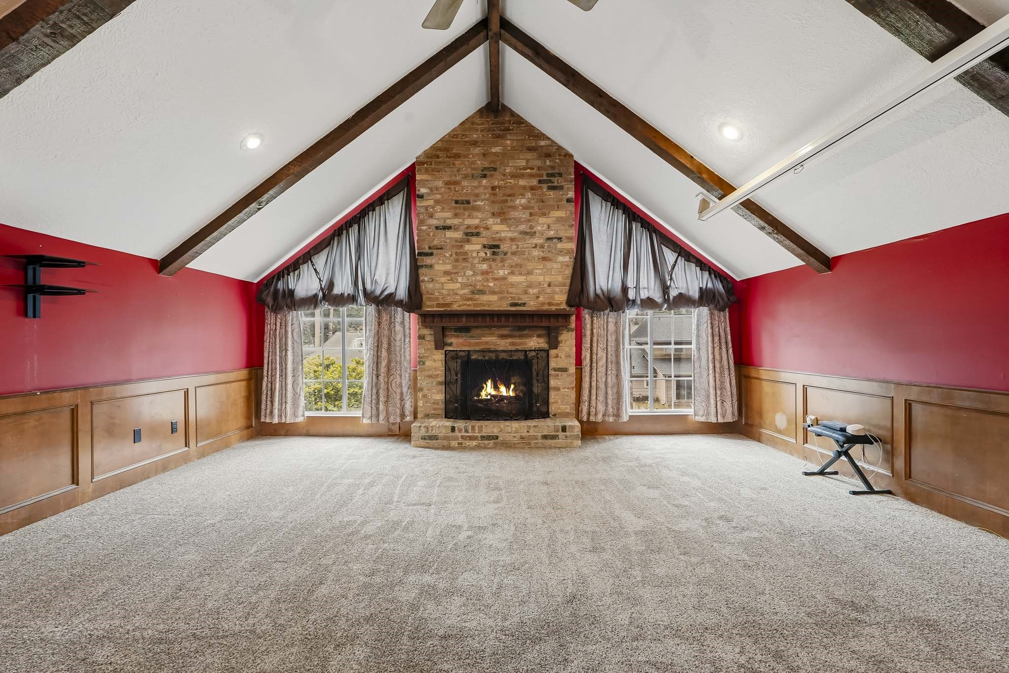 Spacious game room featuring a dramatic vaulted ceiling with exposed beams, a cozy brick fireplace, and walls complemented by elegant wood paneling.