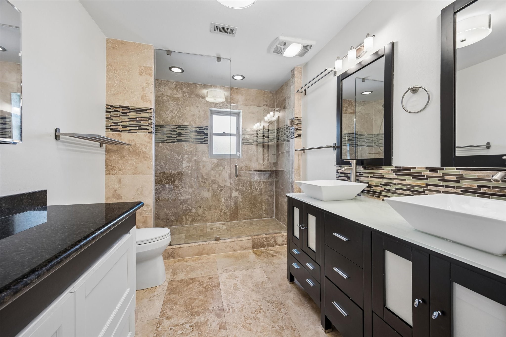 The beautiful primary bath features a seamless glass shower with built-in shelving, double sinks, and an additional vanity with clever integrated storage.