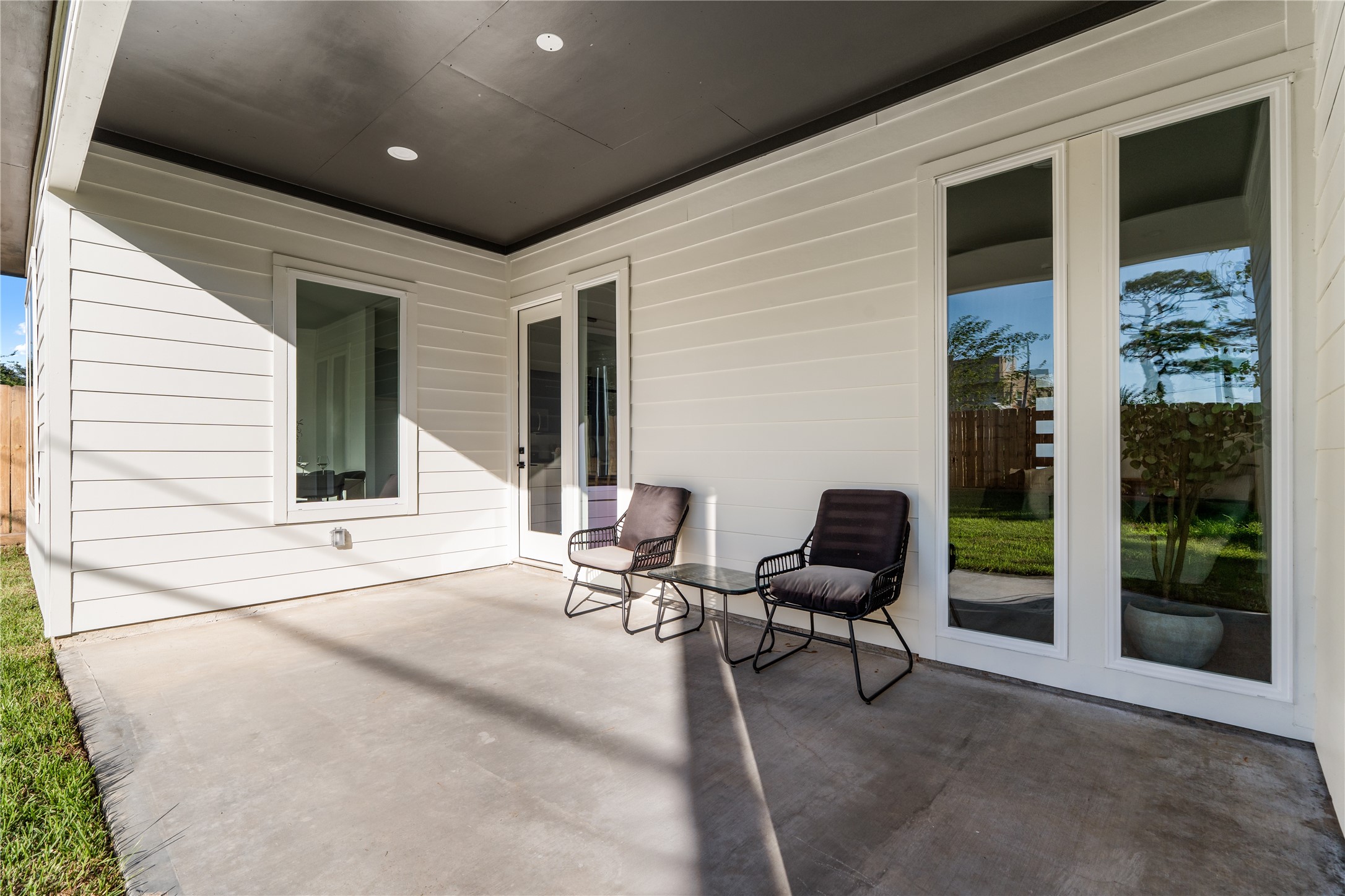 An inviting covered patio with expansive windows and a glass-paneled door create a natural connection between the interior and surrounding backyard.