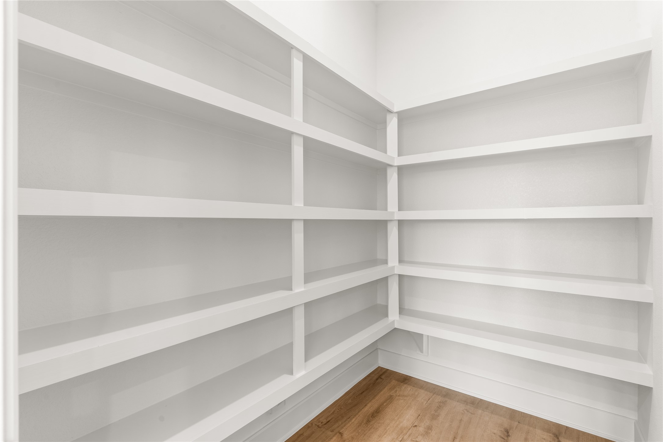 A generously appointed walk-in pantry offers extensive built-in shelving across multiple walls, providing dedicated storage for dry goods, kitchen essentials, and small appliances.