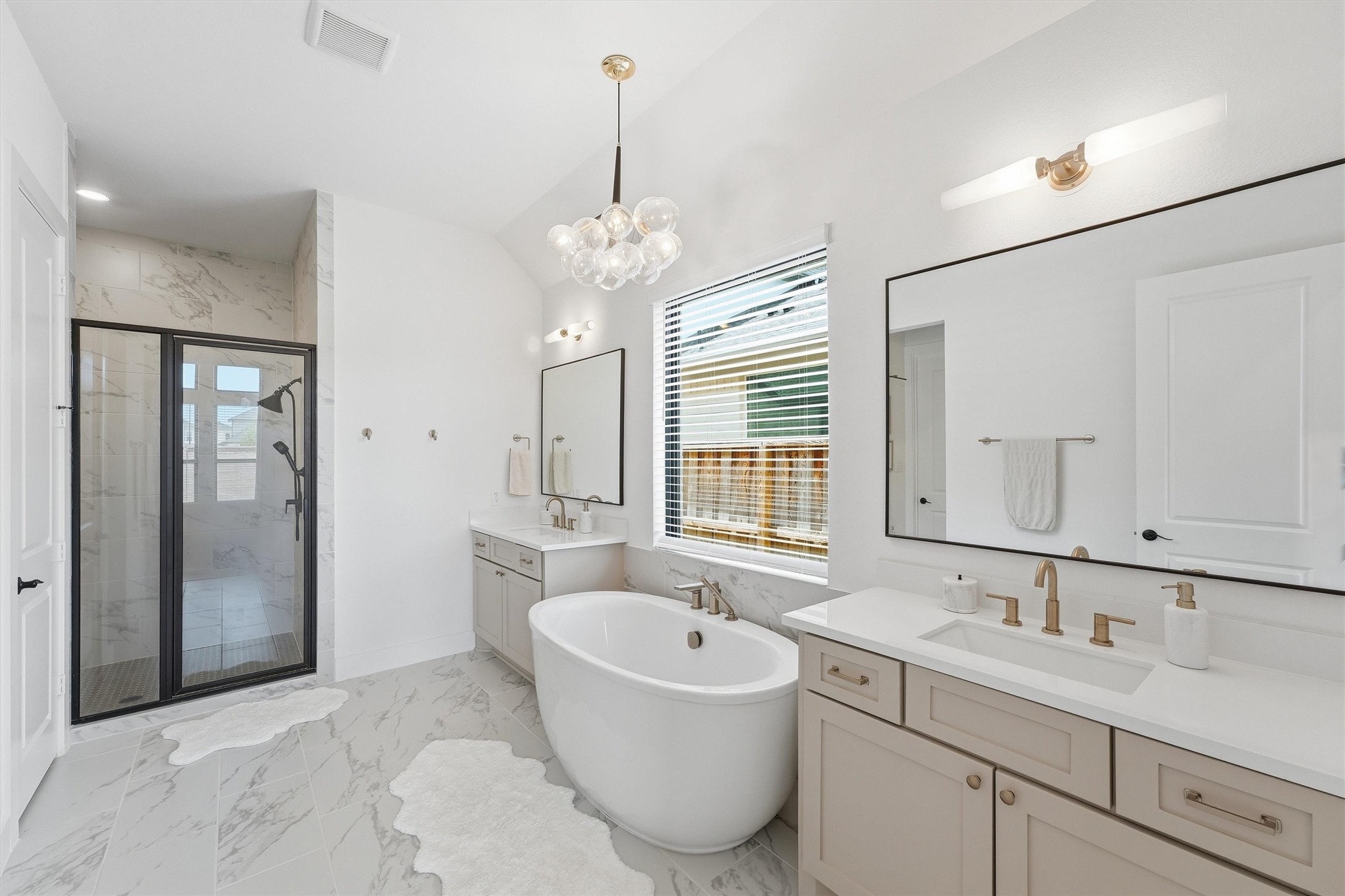 Experience the epitome of luxury in this spa-inspired primary bathroom, featuring a freestanding soaking tub, oversized walk-in shower, and dual vanities, all adorned with elegant marble-look tile and accented by sophisticated gold fixtures and designer lighting.