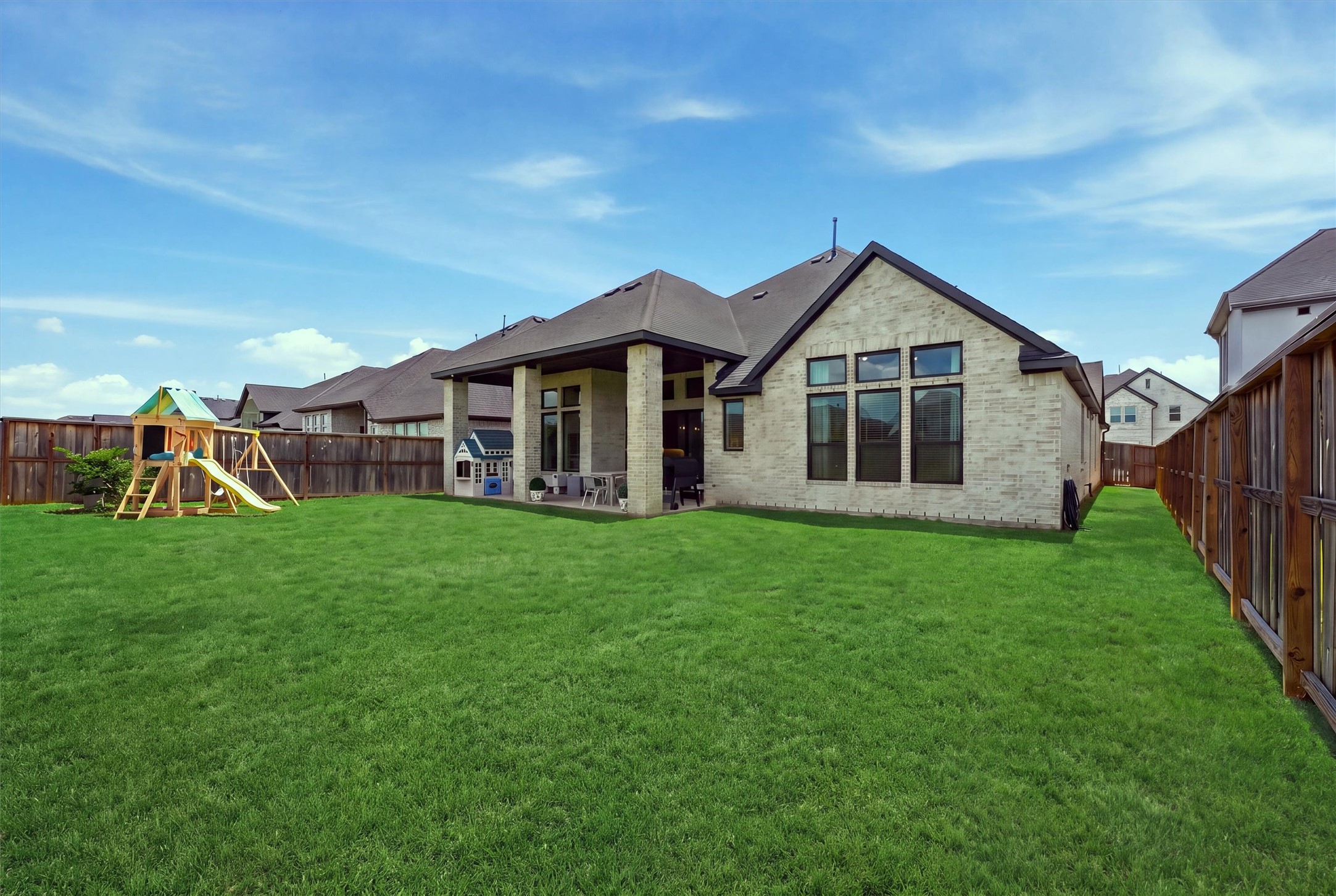 Experience the perfect blend of elegance and outdoor living with this home's expansive backyard featuring a stunning covered patio, light brick facade, large windows, and lush greeneryideal for entertaining, play, or adding a future pool.
