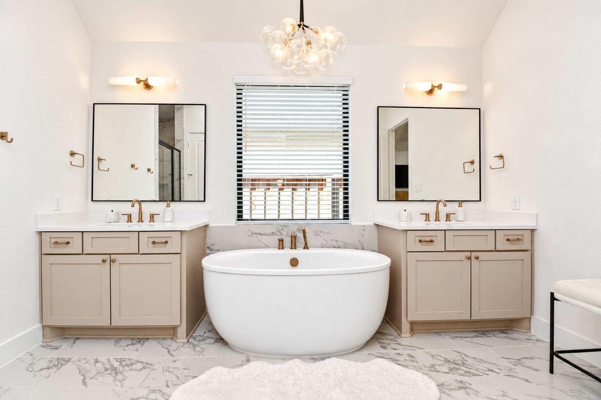 Luxurious bathroom featuring a freestanding soaking tub, dual vanities with elegant gold fixtures, and chic lighting, all complemented by marble like flooring and modern accents.
