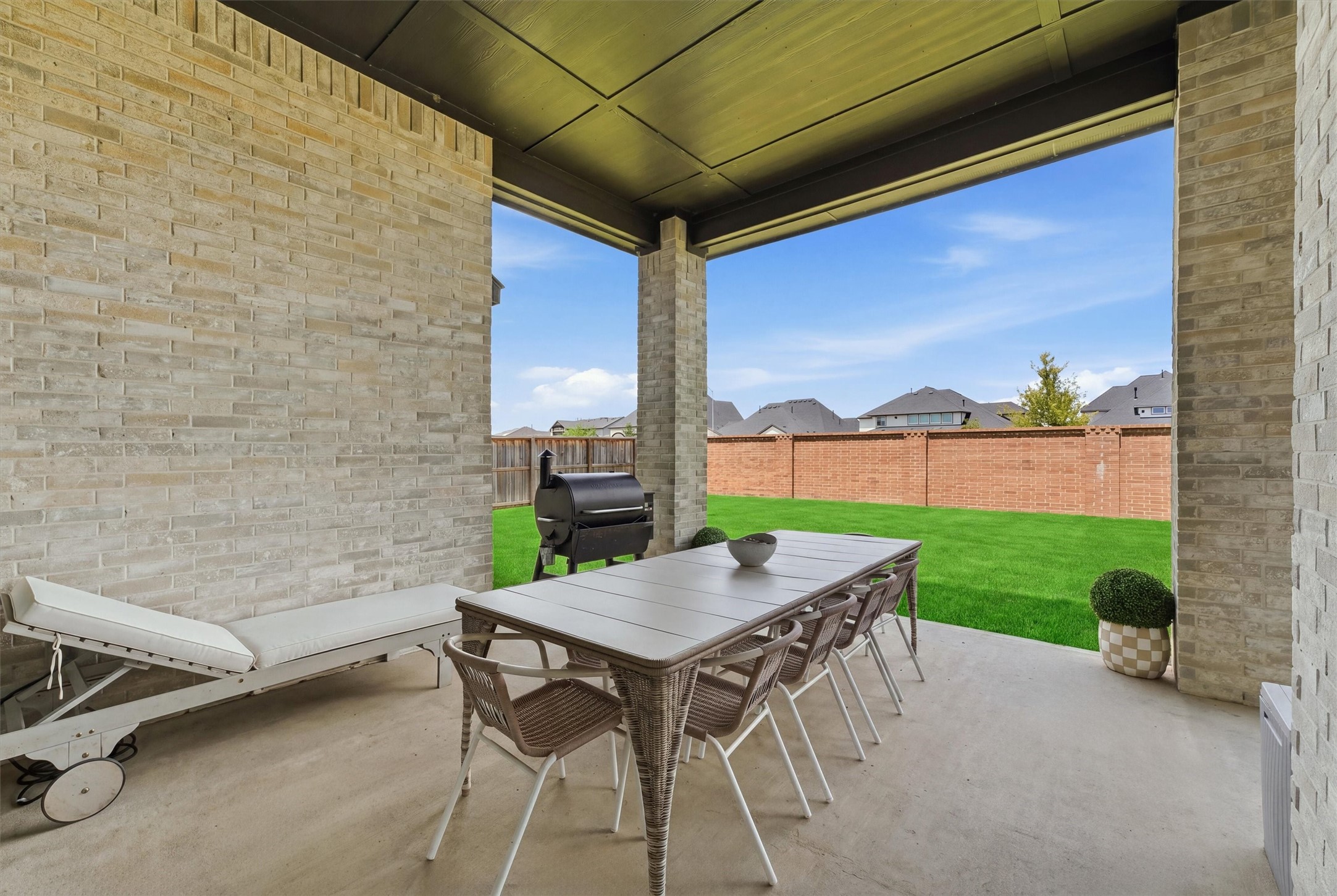Spacious covered outdoor patio overlooking a beautifully maintained backyard, offering plenty of room for dining, lounging, grilling, and entertaining. The brick privacy wall and generous green space create a private, relaxing setting perfect for enjoying the outdoors year round.