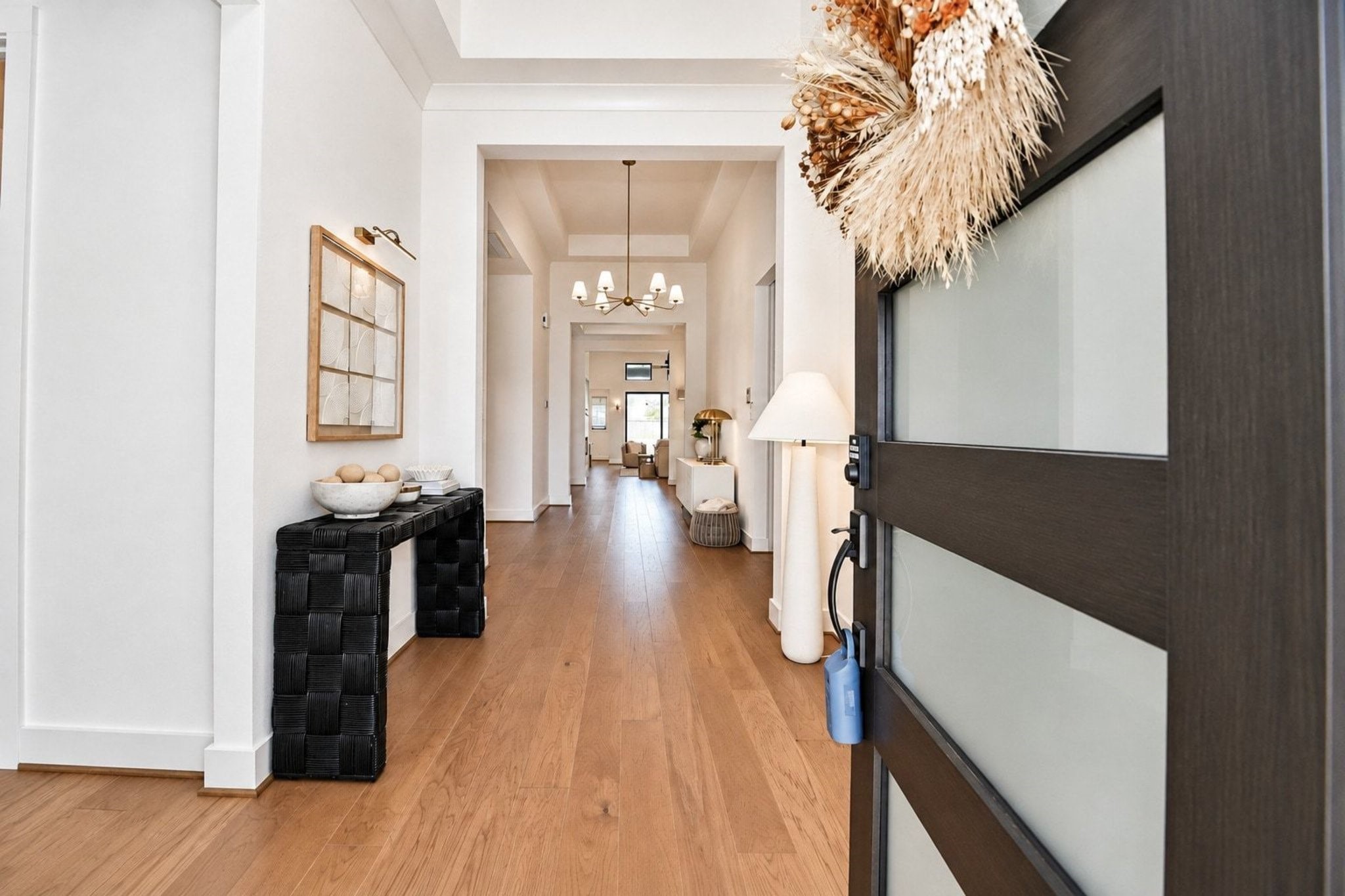 Step into a bright and welcoming entryway with elegant wood flooring, modern decor, and a stylish light fixture leading to an open and inviting living space.