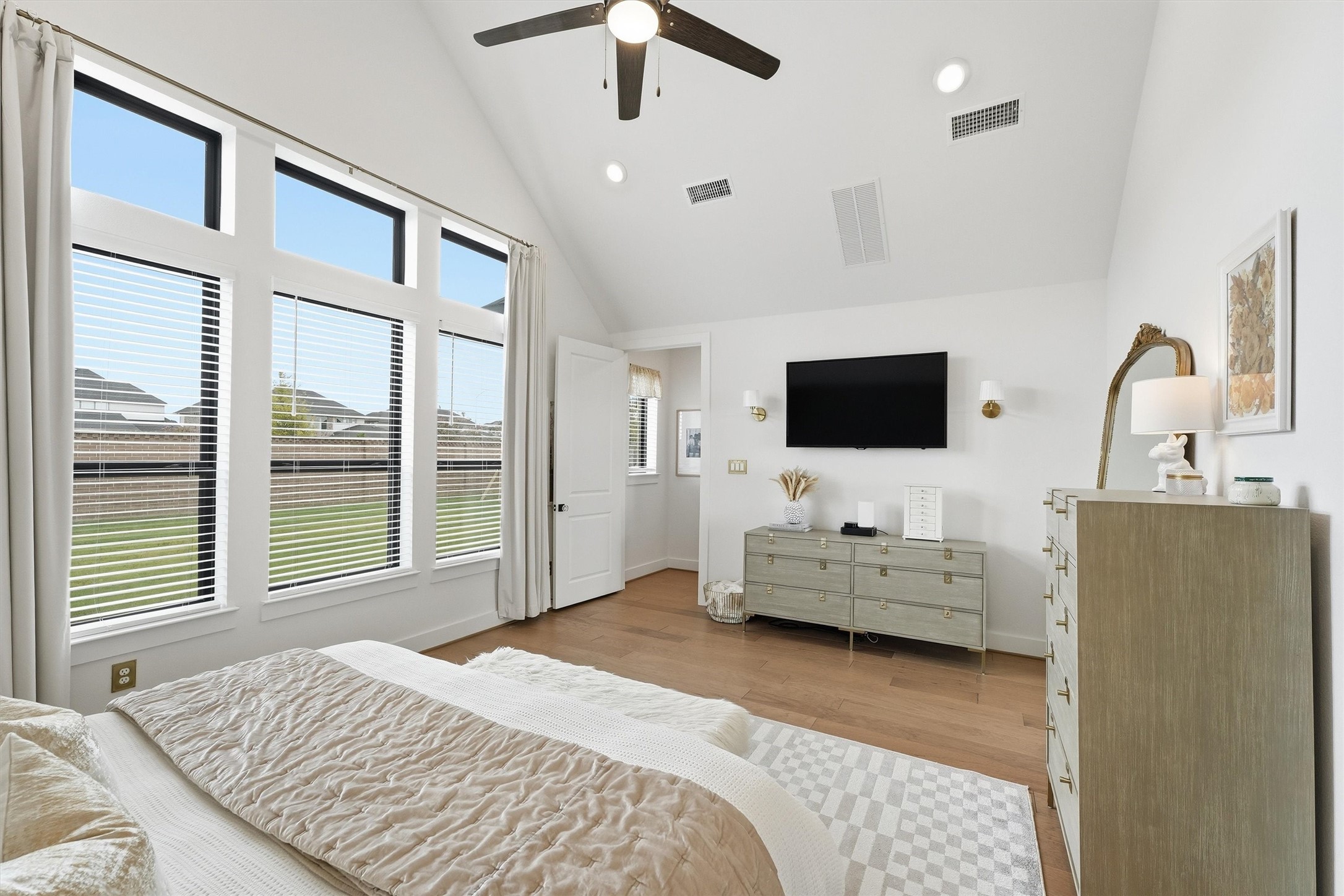 A serene primary bedroom retreat with soaring ceilings and modern finishes, bathed in natural light from oversized windows offering beautiful backyard views, creates a bright and relaxing atmosphere.