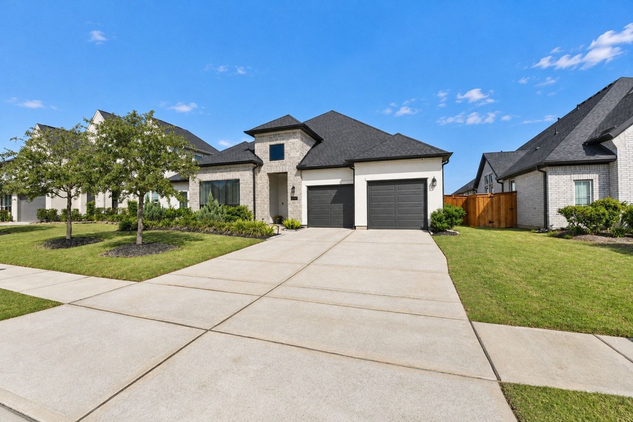 Modern single-story home with a sleek black roof, three-car tandem garage, and well-manicured lawn, offering great curb appeal.