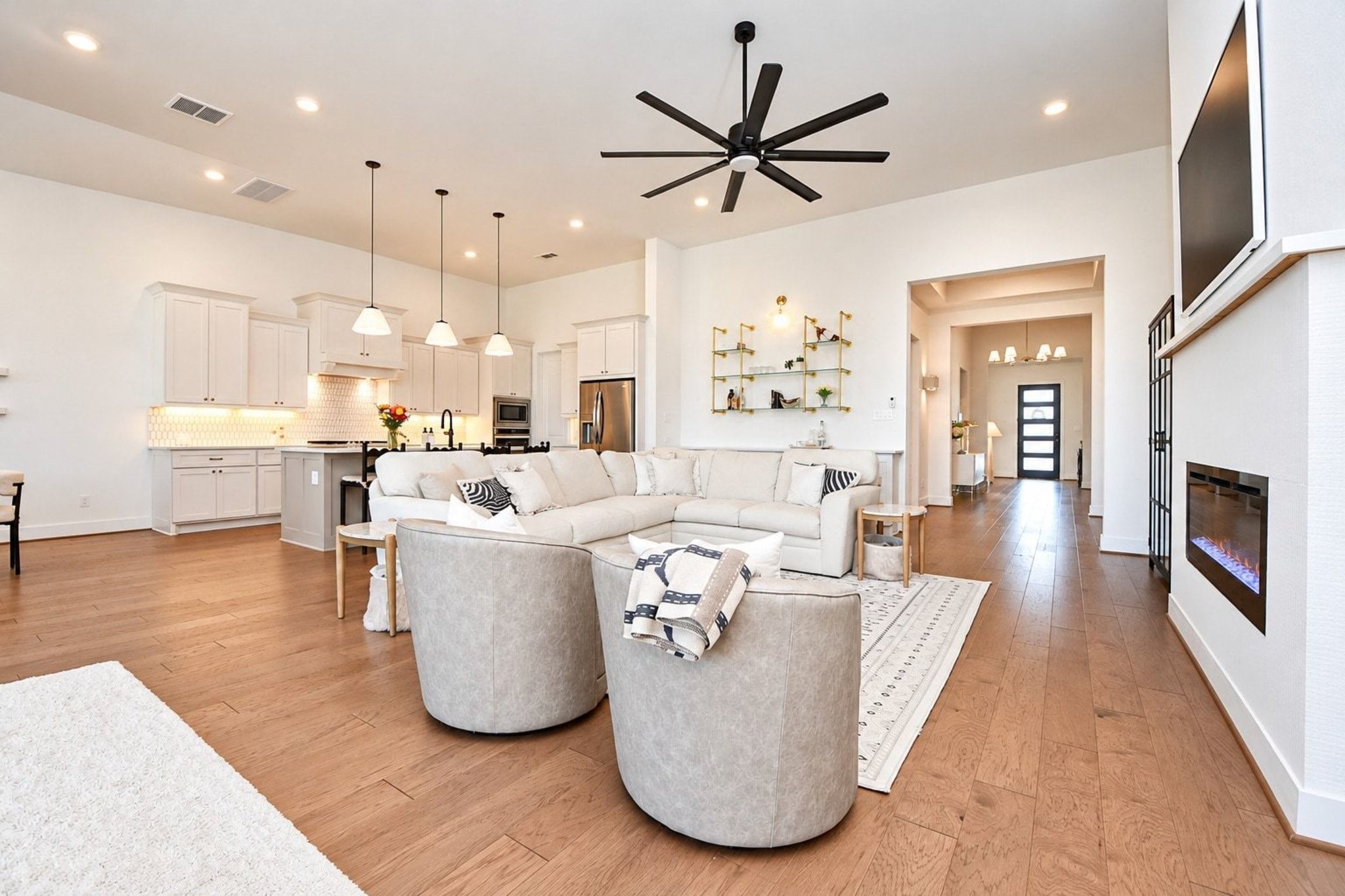 Spacious open-concept living area with modern kitchen, elegant light fixtures, and a cozy fireplace, perfect for entertaining.