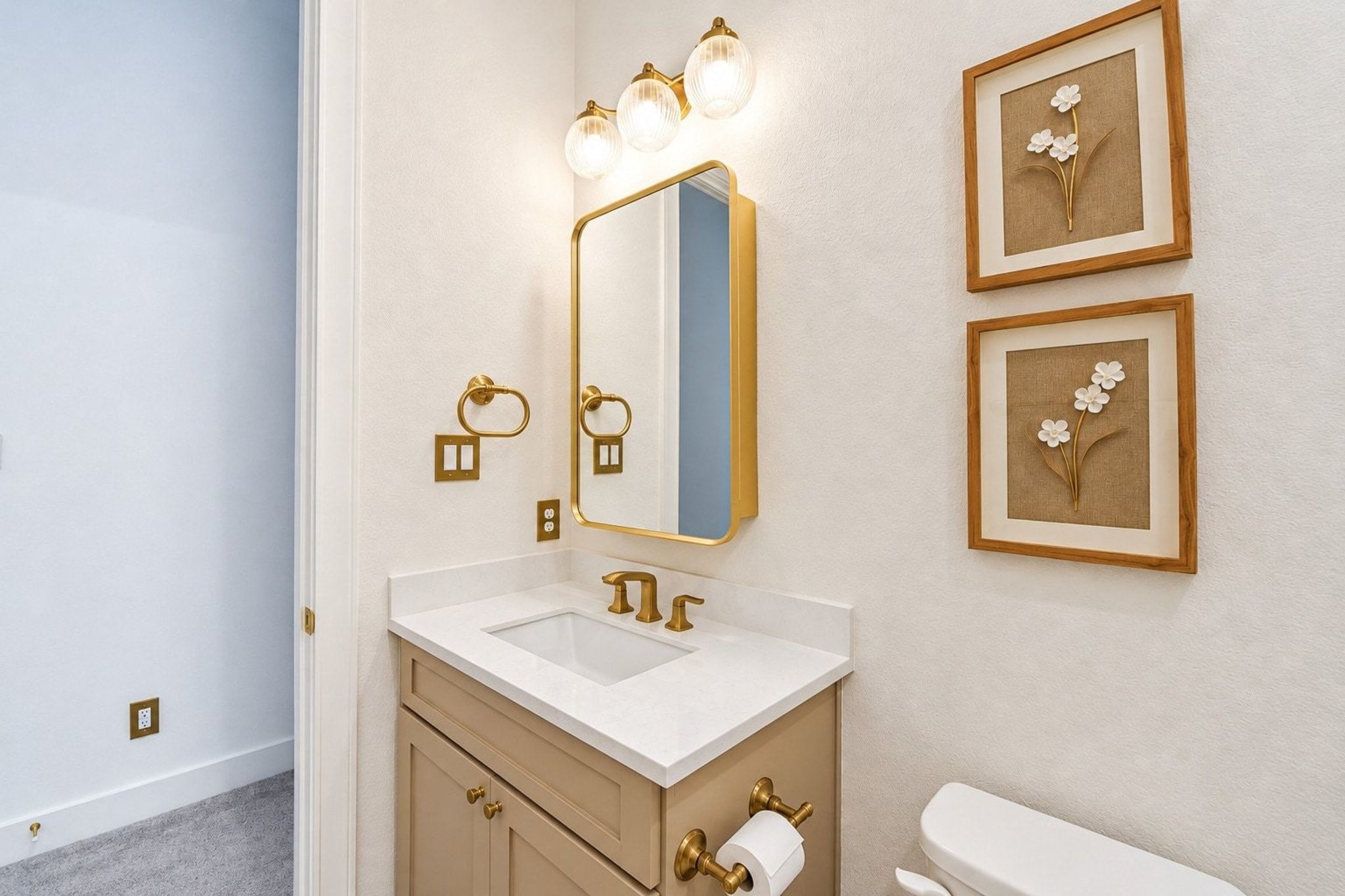 Chic bathroom with elegant gold fixtures, a sleek vanity with upgraded lighting, and tasteful floral artwork, offering a sophisticated and inviting atmosphere.