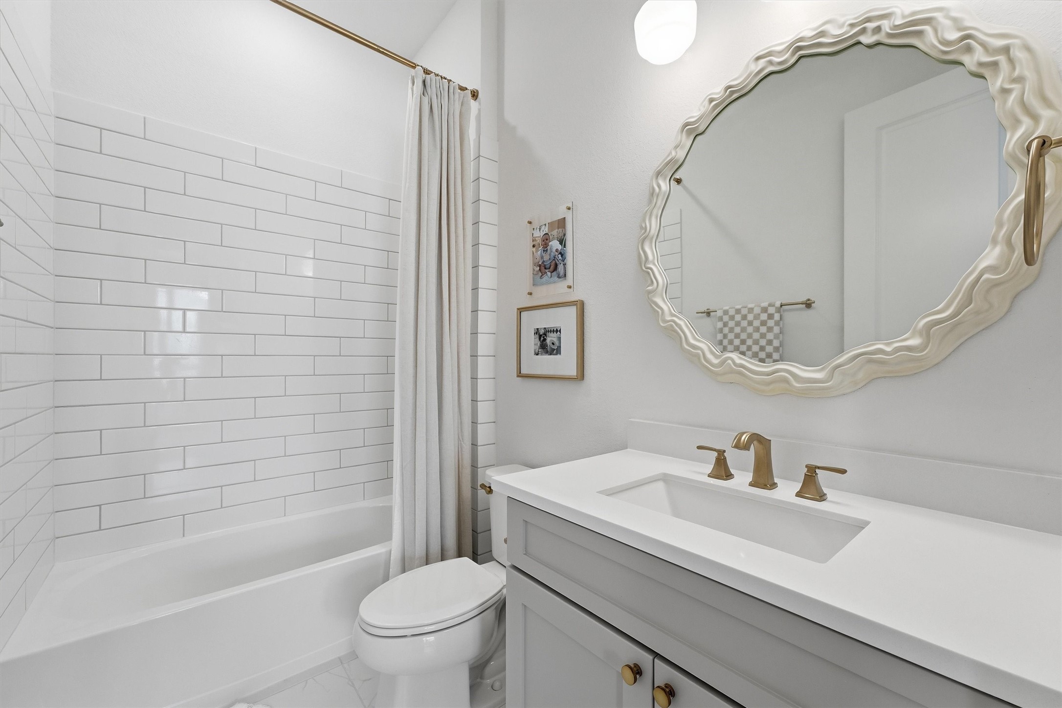 A stylish secondary bathroom featuring classic white subway tile, a sleek vanity, and warm gold fixtures. The statement mirror adds a fun designer touch while keeping the space bright, fresh, and modern.