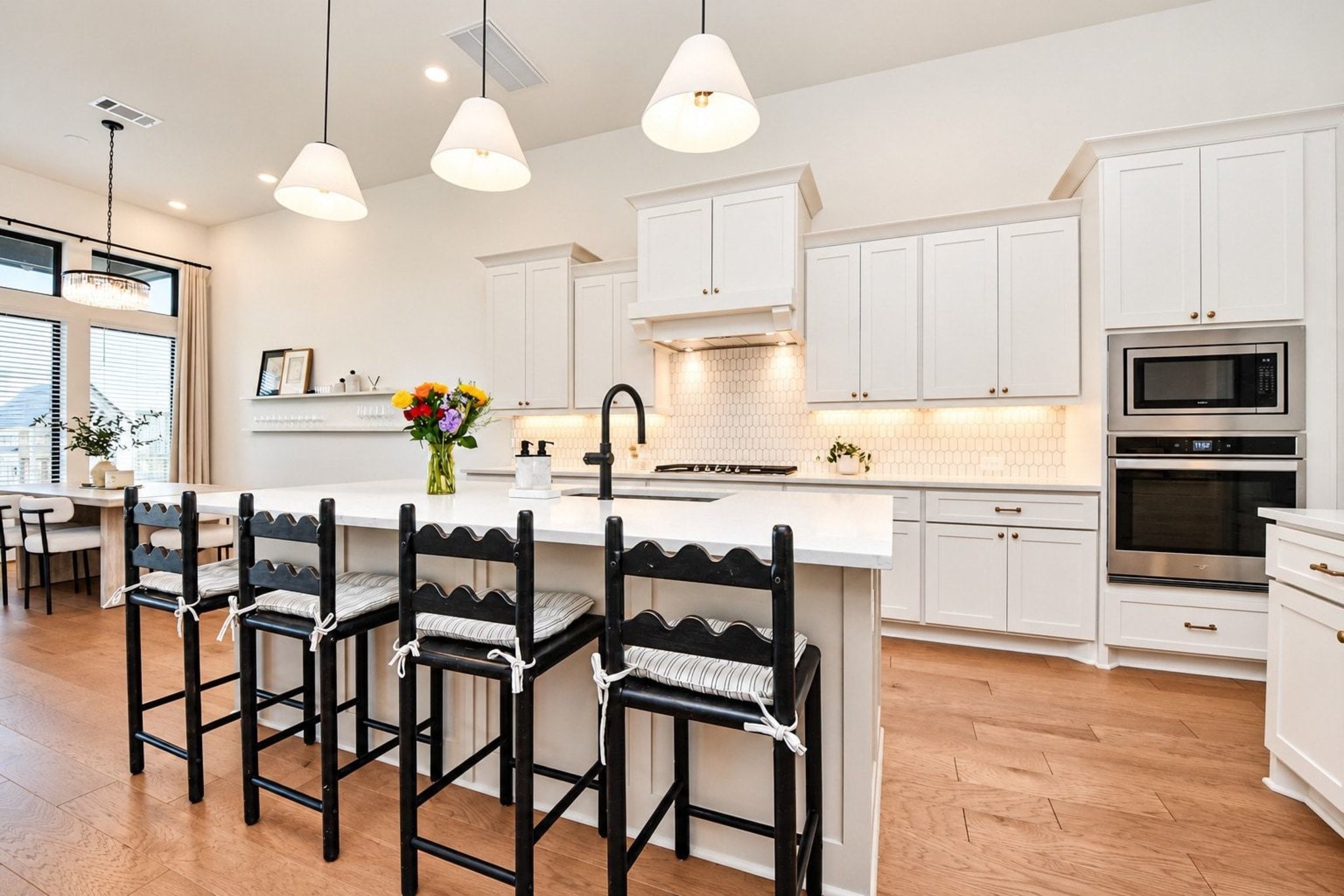 Bright and spacious kitchen featuring sleek white cabinetry, stainless steel appliances, upgraded pendent lights that cover a large island with seating, perfect for entertaining.