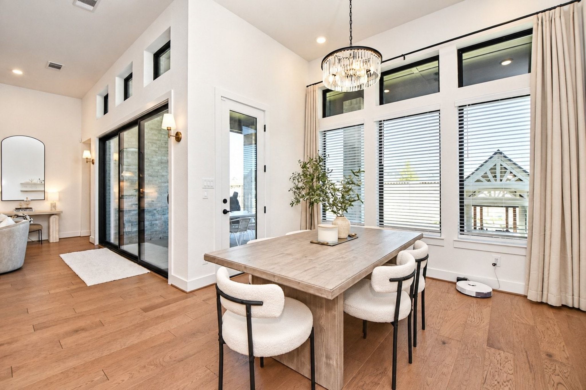 Bright and airy dining area featuring large windows, high ceilings, elegant chandelier, and a seamless flow into the living space.