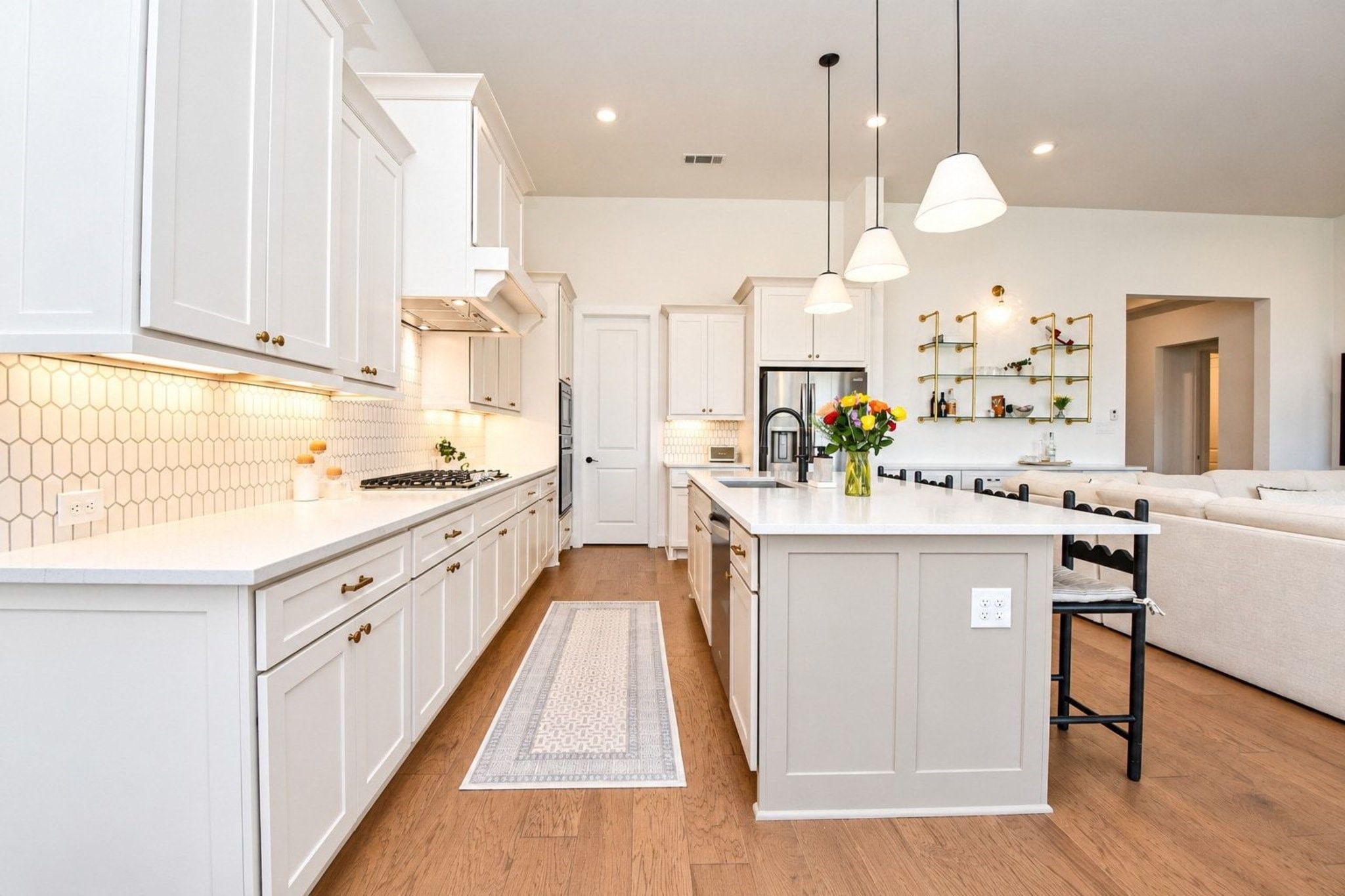 Spacious and modern kitchen featuring sleek white cabinetry, a large central island with pendant lighting, and elegant hardwood floors. The open design seamlessly connects to the living area, ideal for entertaining.