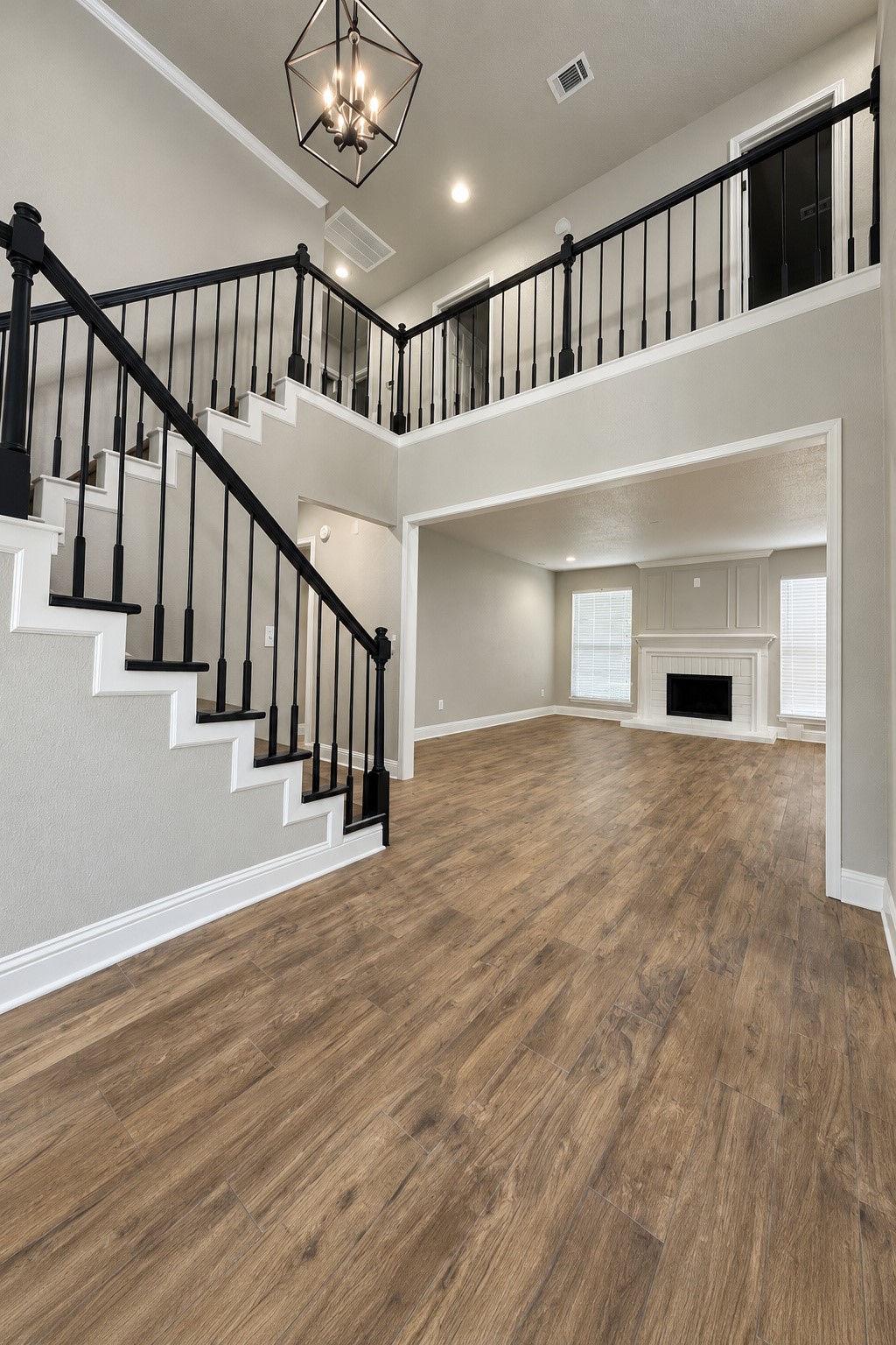 Beautiful two-story entry featuring an elegant staircase with black railings, rich wood-look flooring, and an open view into the spacious living room with fireplace.