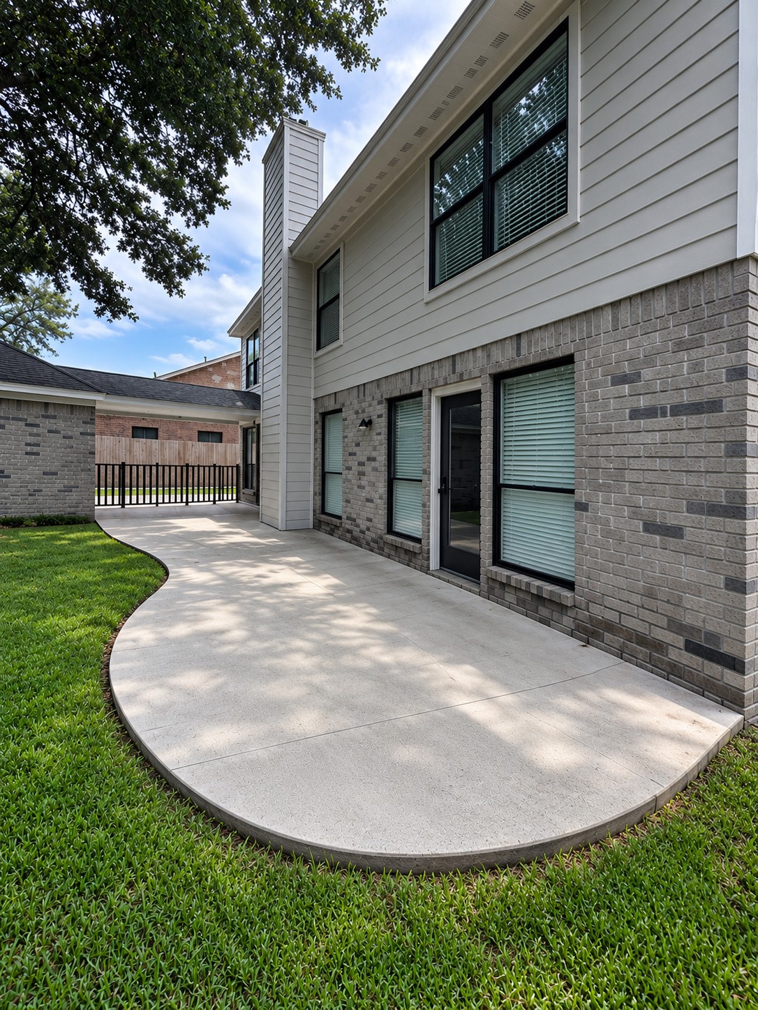 Spacious curved concrete patio overlooking the backyard, shaded by mature trees.