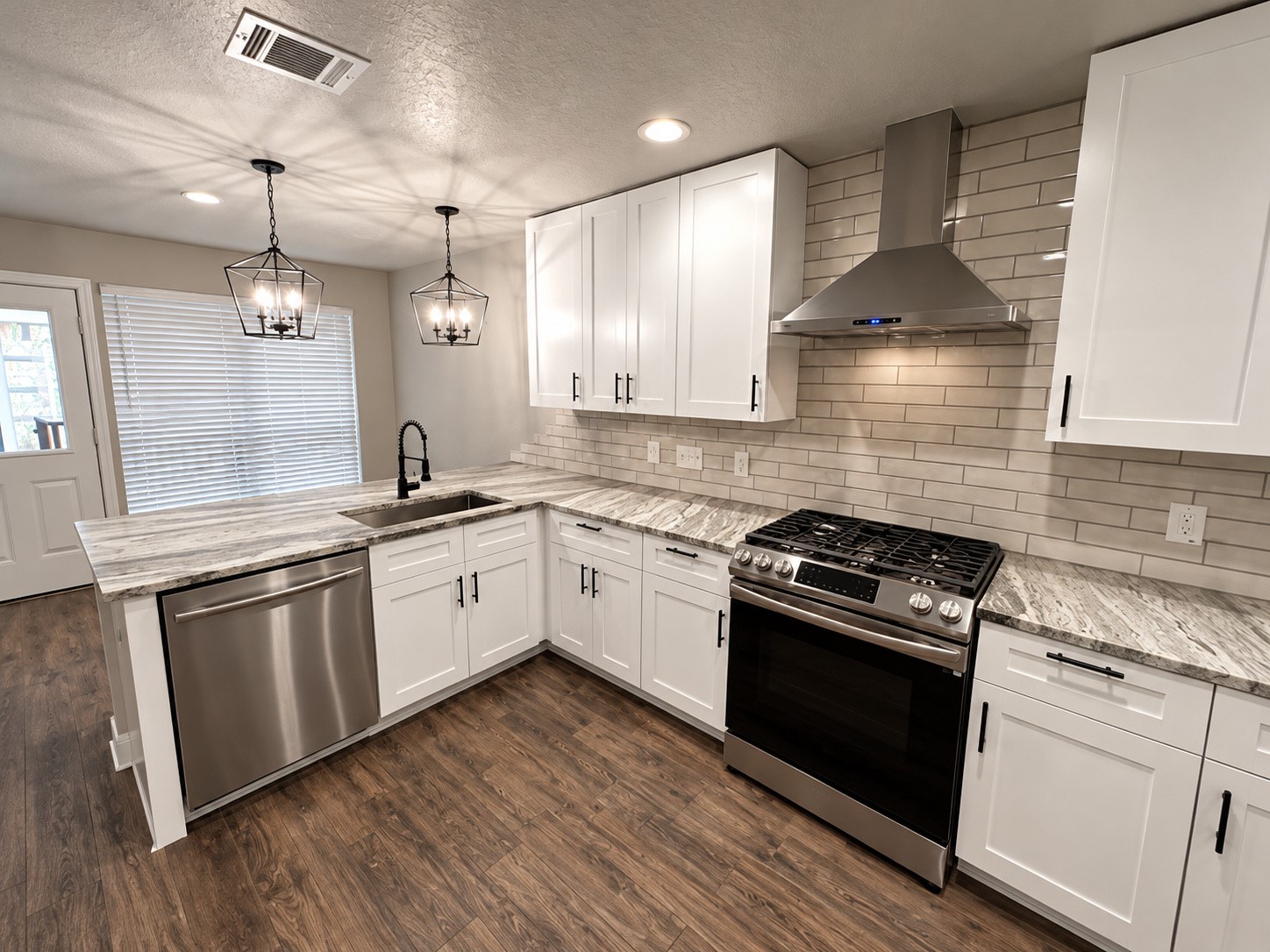 Beautifully remodeled kitchen featuring white shaker cabinets, granite countertops, stainless steel appliances, and stylish modern lighting.