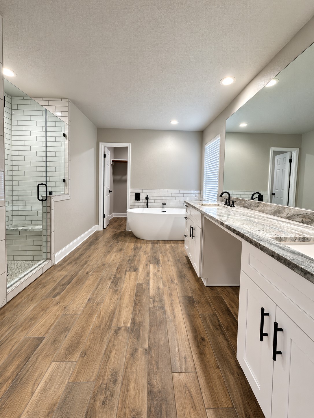 Luxuriously renovated primary bathroom featuring a freestanding soaking tub, spacious walk-in shower, dual vanities, elegant modern finishes, and a large walk-in primary closet.