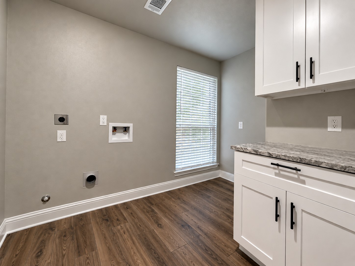 Spacious laundry room with built-in cabinetry, countertop workspace, natural lighting, and room for an additional refrigerator or freezer.