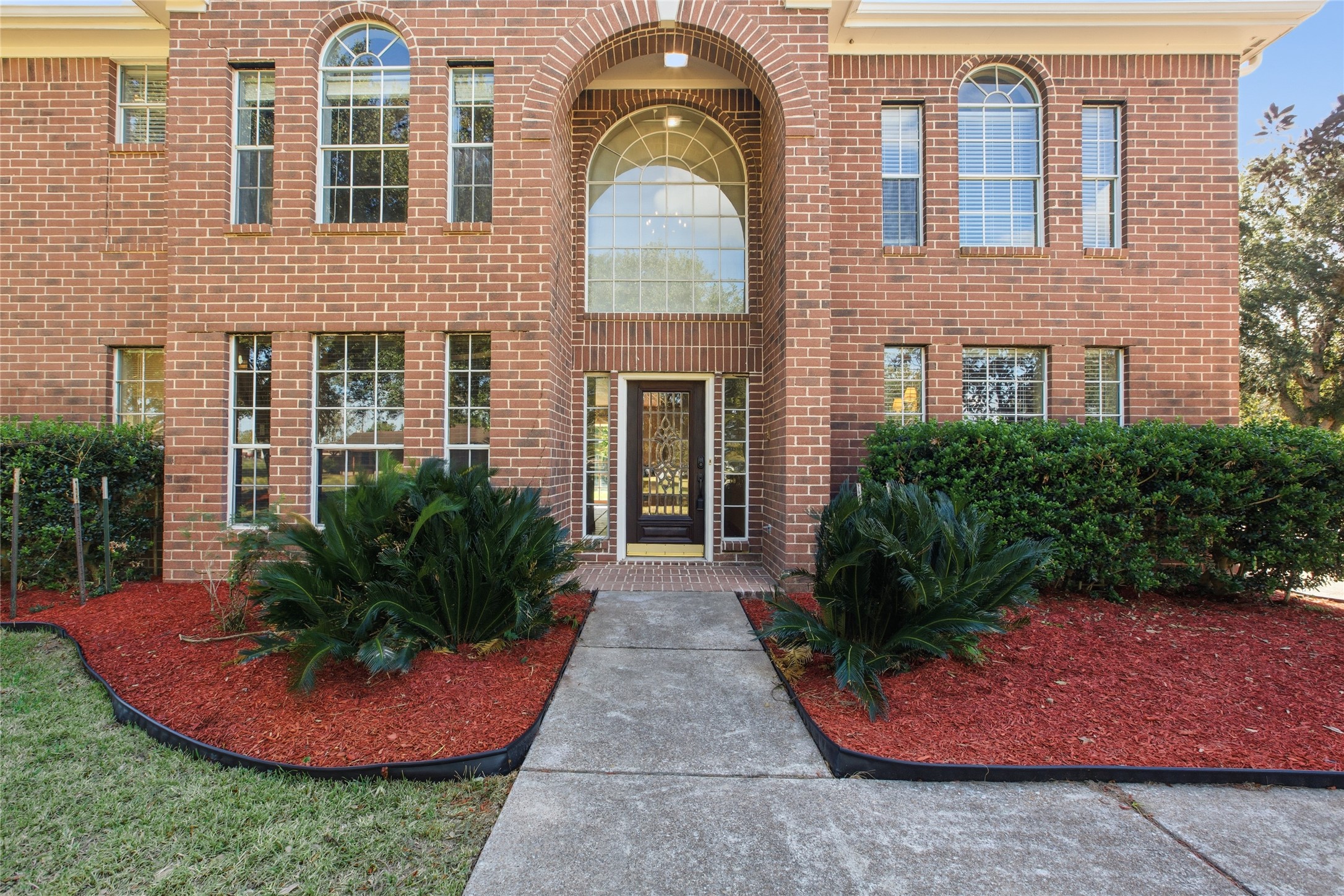 Two-story brick home in Alvin TX with arched entry and landscaped front beds Two-story brick home in Alvin TX with arched entry and landscaped front beds