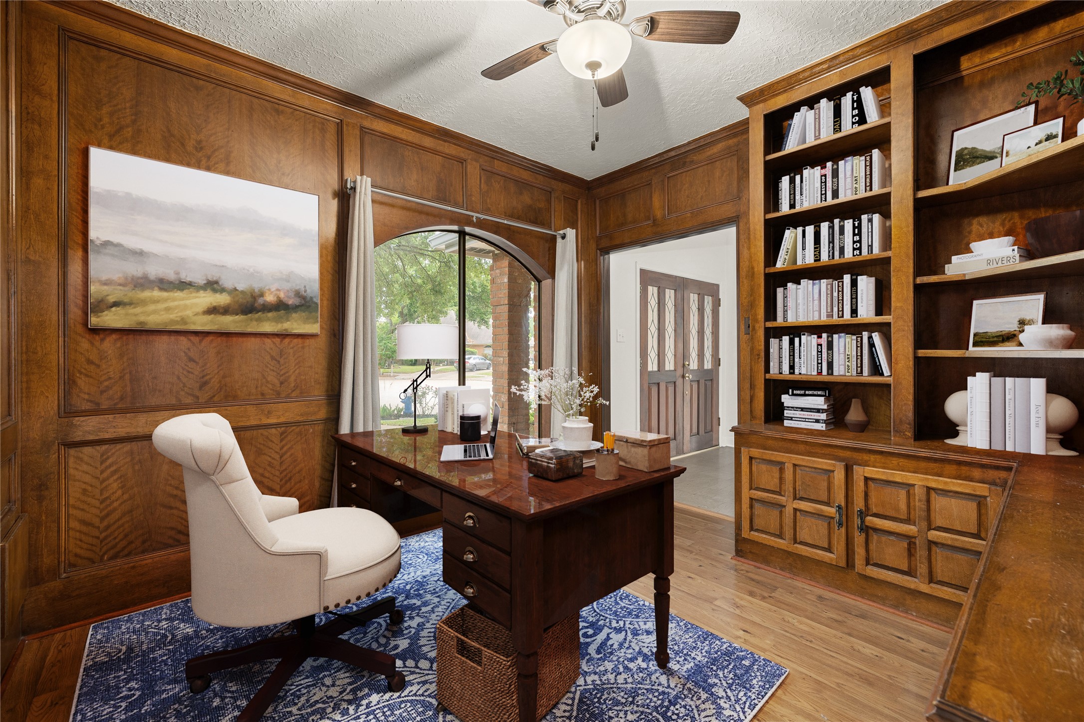 Quietly nestled in front of the home is the handsome home office! Featuring wood flooring, high ceilings, large arched window, ceiling fan, custom paint, and a large built-in bookcase! *Virtually Staged