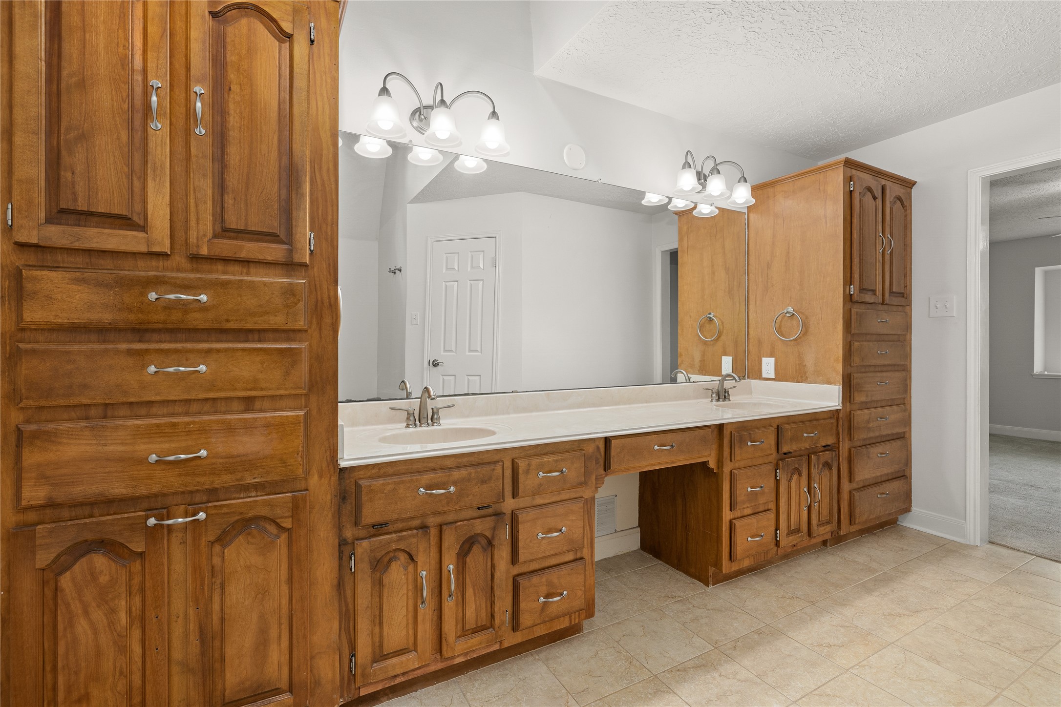 The primary bathroom offers a spa-like retreat with an expansive double vanity and an abundance of custom storage. This well-appointed space features warm wood cabinetry and a thoughtful layout designed for both luxury and daily convenience.