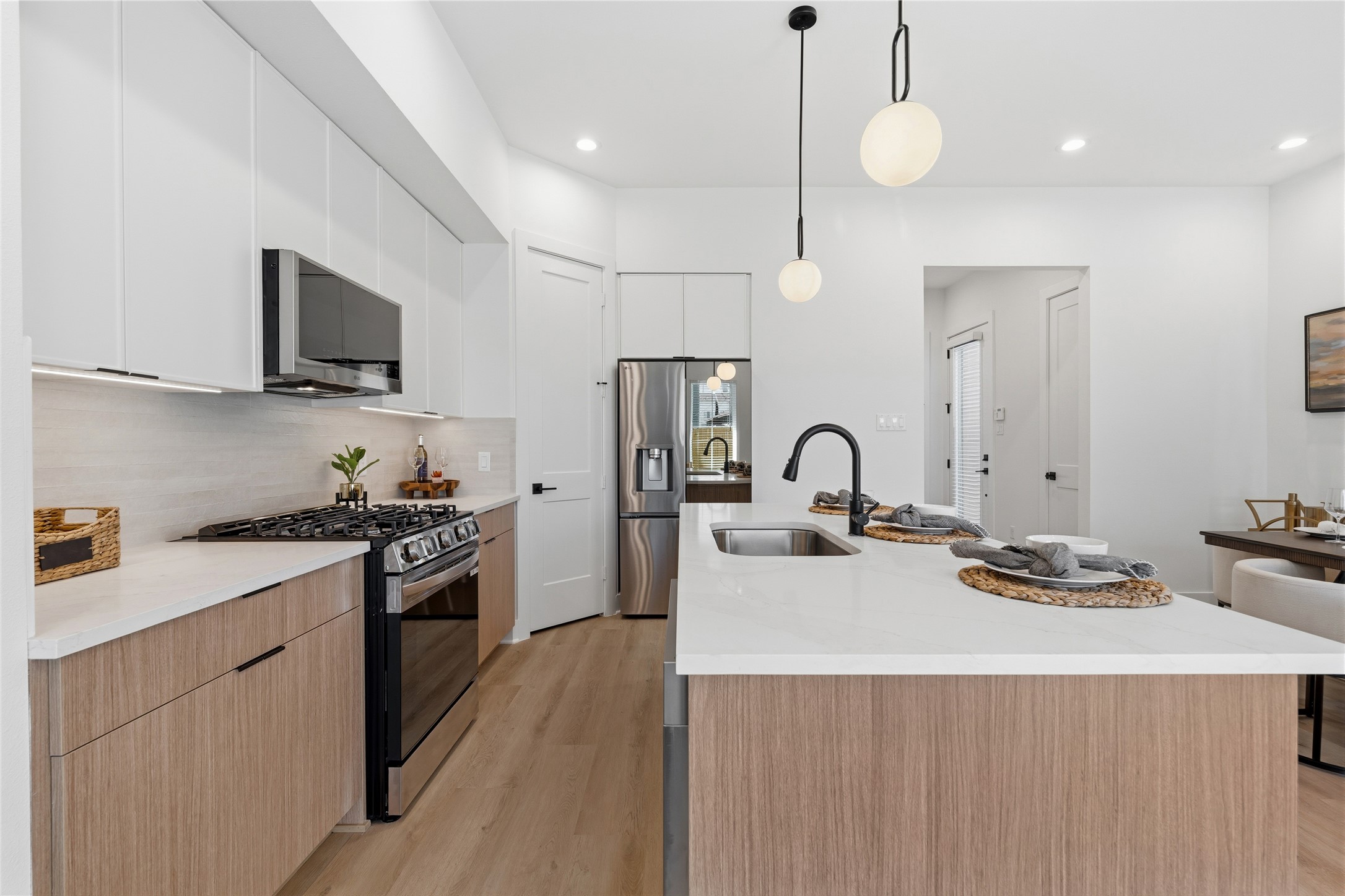 A large island with a white quartz contertops serves as the rooms anchor. Matte black fixtures and integrated stainless steel appliances provide a modern, high-contrast finish.