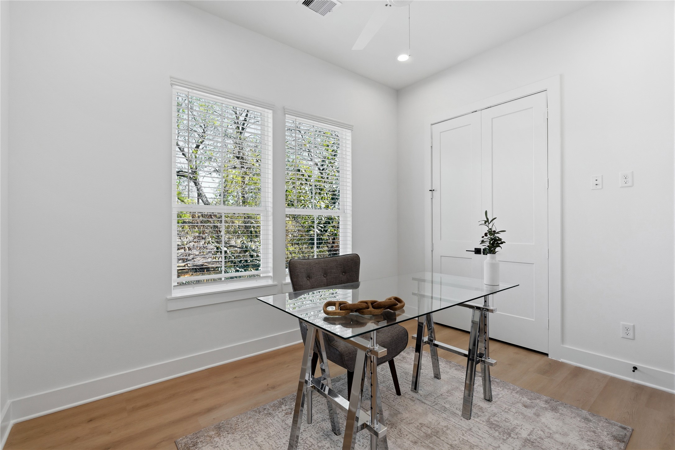 Dual windows provide ample natural light to this crisp, white-walled workspace. Continuous wide-plank flooring and high ceilings maintain the home's airy architectural theme.