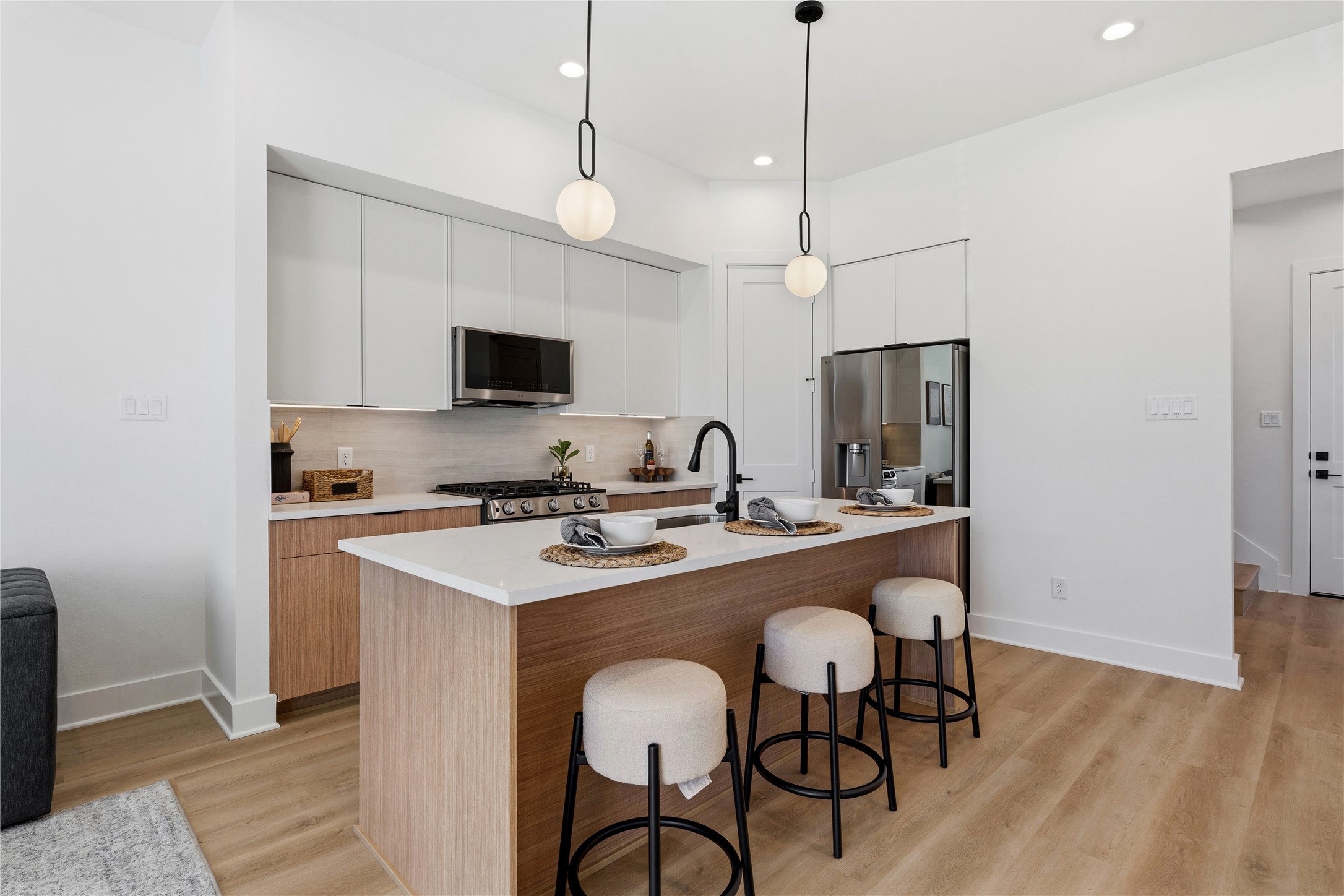 This space features two-tone cabinetry and a large stone-topped island. Minimalist pendants and integrated appliances highlight the clean, functional geometry.