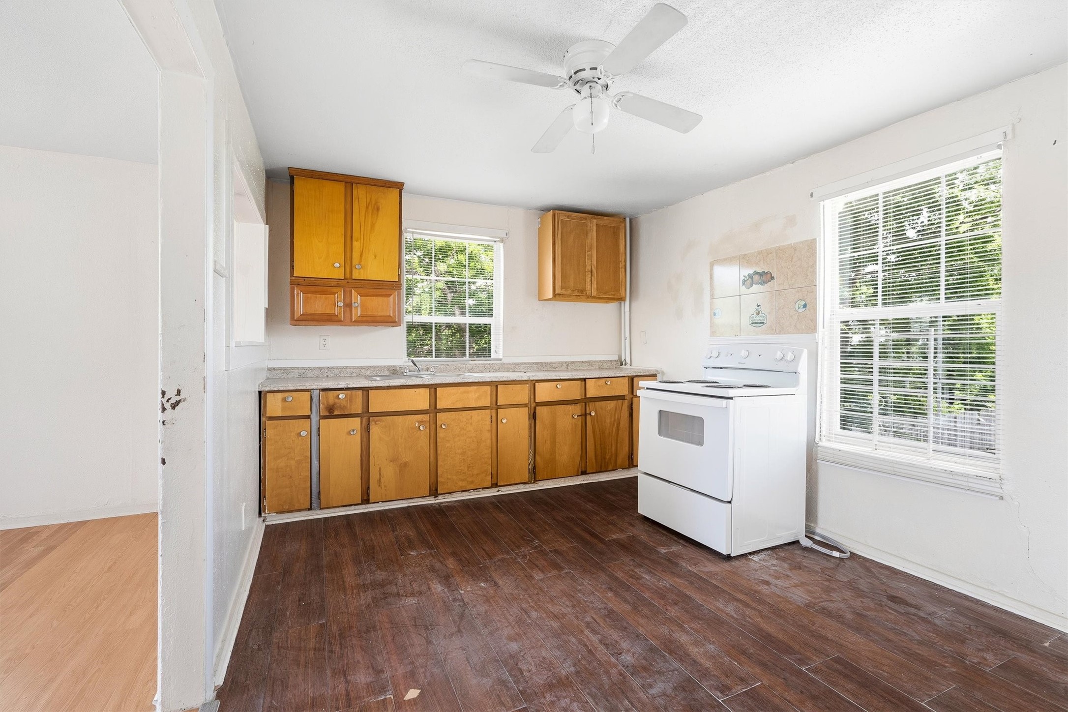 The first floor unit kitchen features stylish laminate flooring, a ceiling fan, and a large window with privacy blinds, creating a bright, comfortable, and functional space for everyday living.