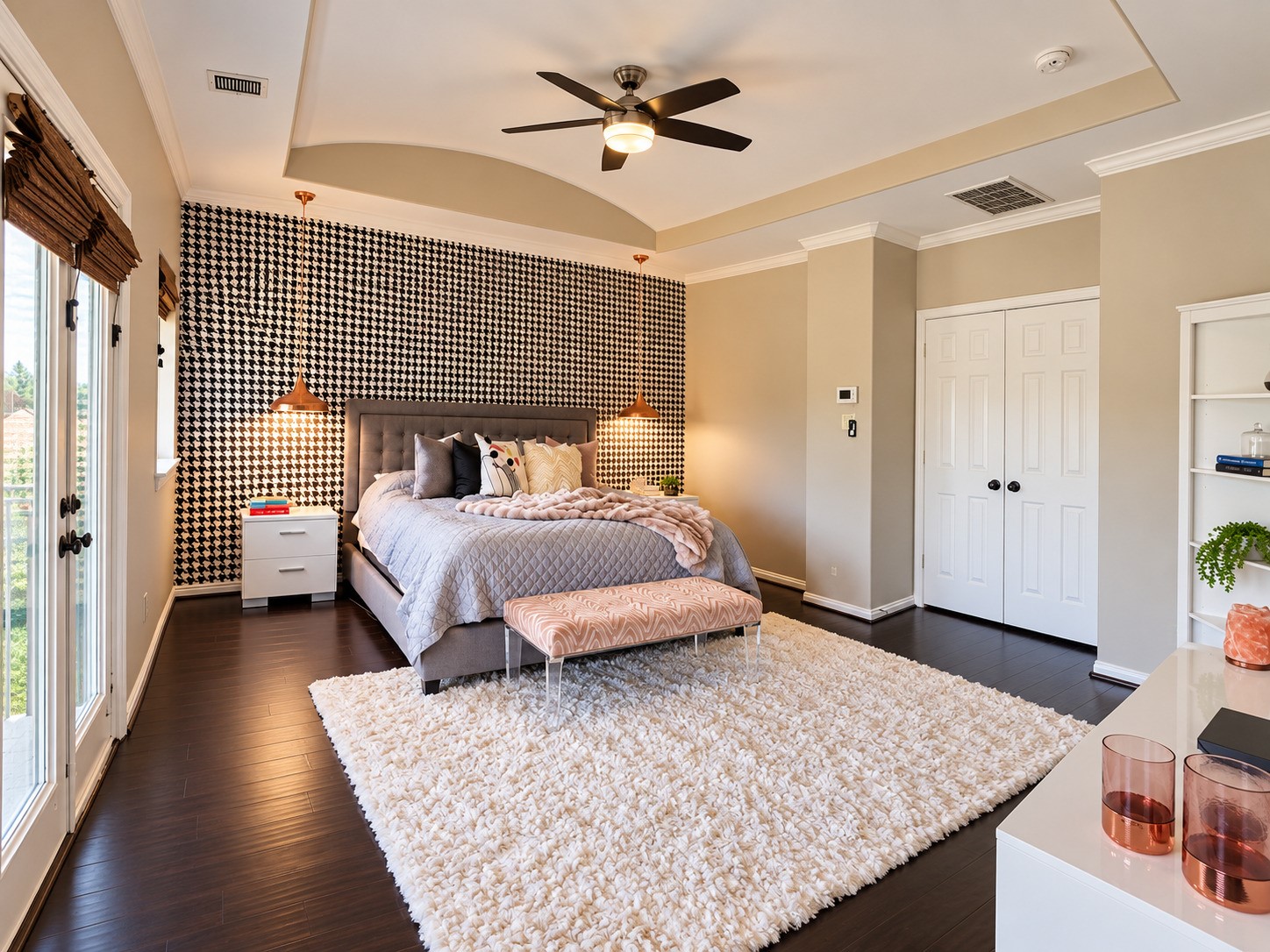 The spacious primary bedroom features hardwood floors, a tray ceiling, designer pendant lights and a striking accent wall.