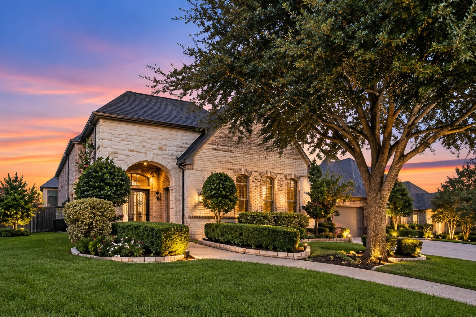 A distinctive stone-and-brick facade features a gated courtyard entry, manicured landscaping and warm architectural lighting.