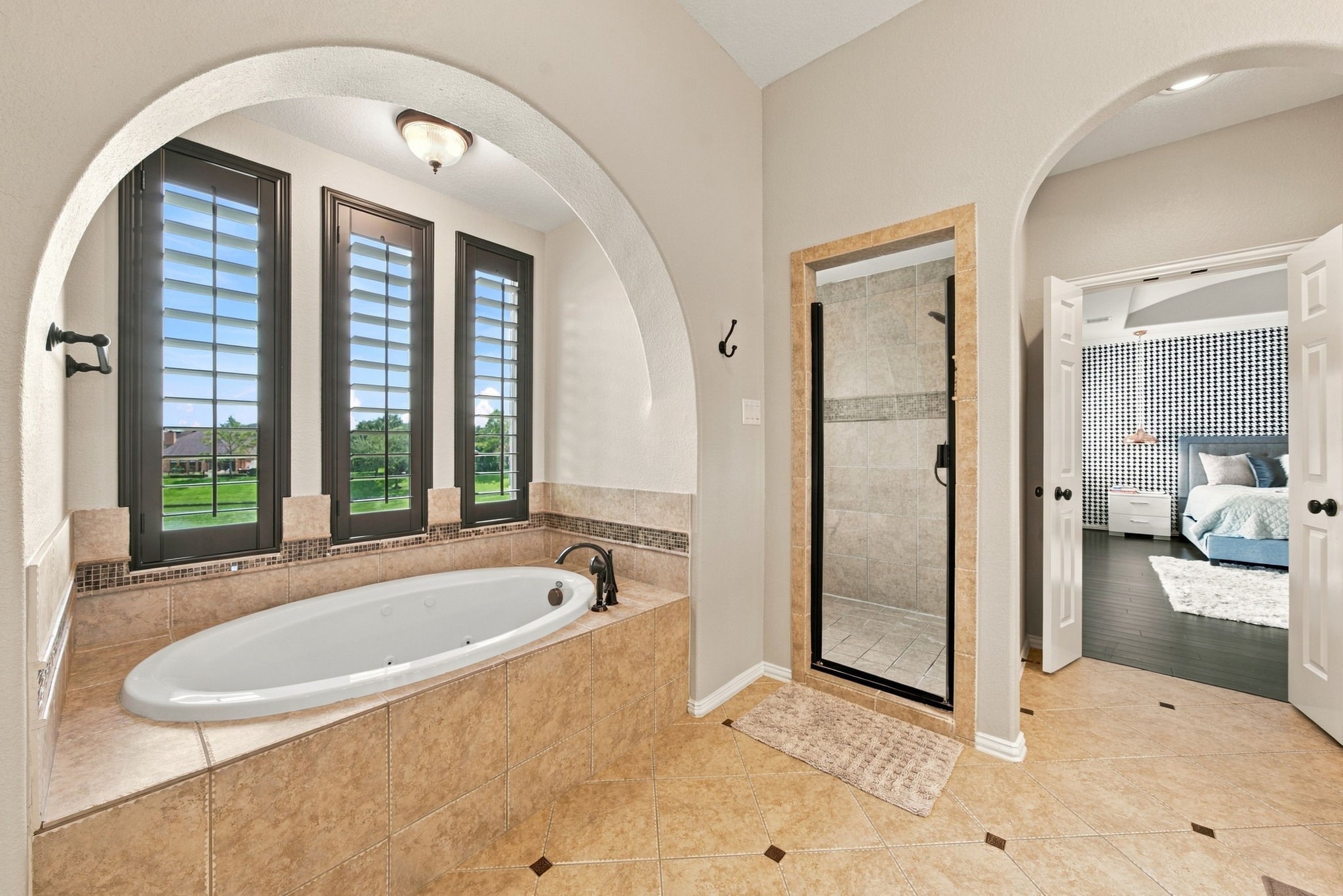 The spacious primary bathroom includes a jetted soaking tub, separate glass-enclosed shower and tall windows overlooking the lake.