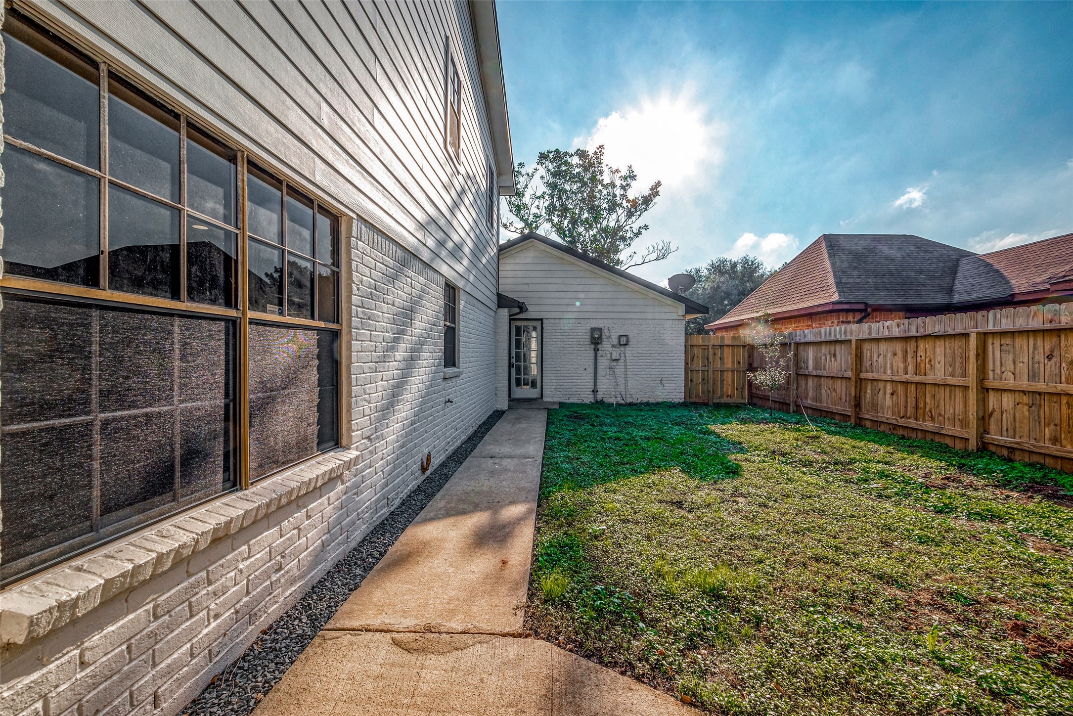 A cozy backyard with a concrete path, grassy area, and a wooden fence.
