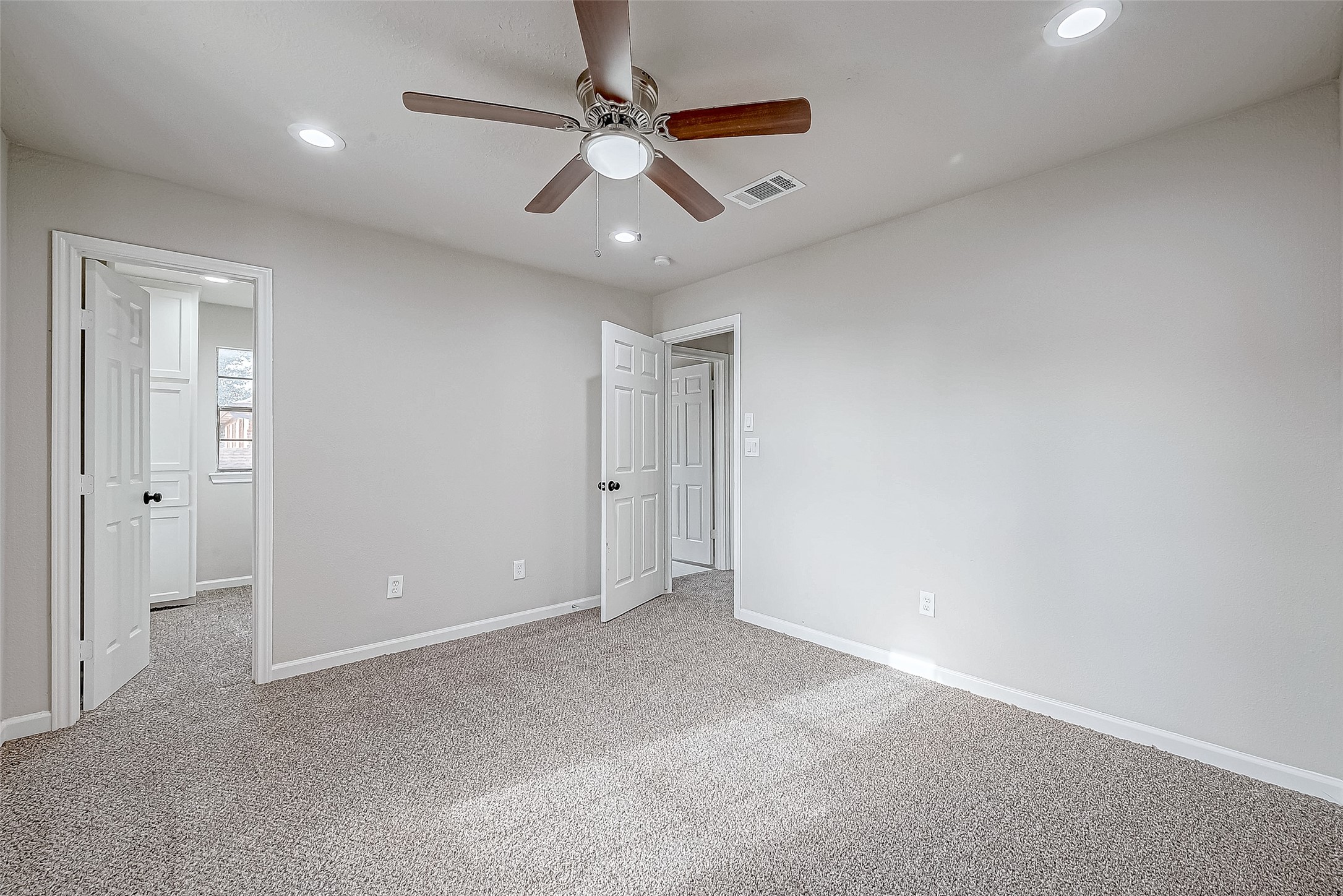 Spacious and inviting bedroom featuring plush carpeting, ample natural light, and a modern ceiling fan.