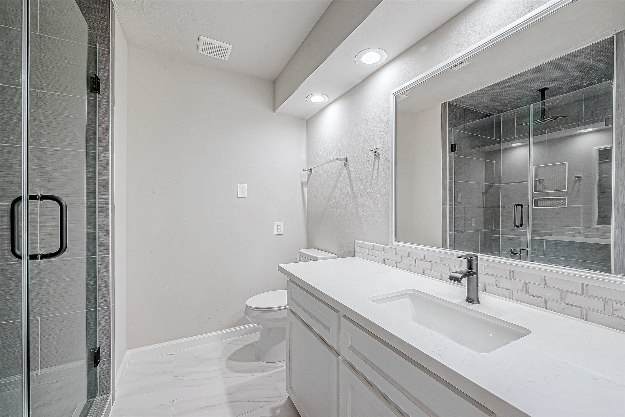 This bathroom features a modern design with a vanity with a contemporary faucet, large mirror and bright overhead lighting.
