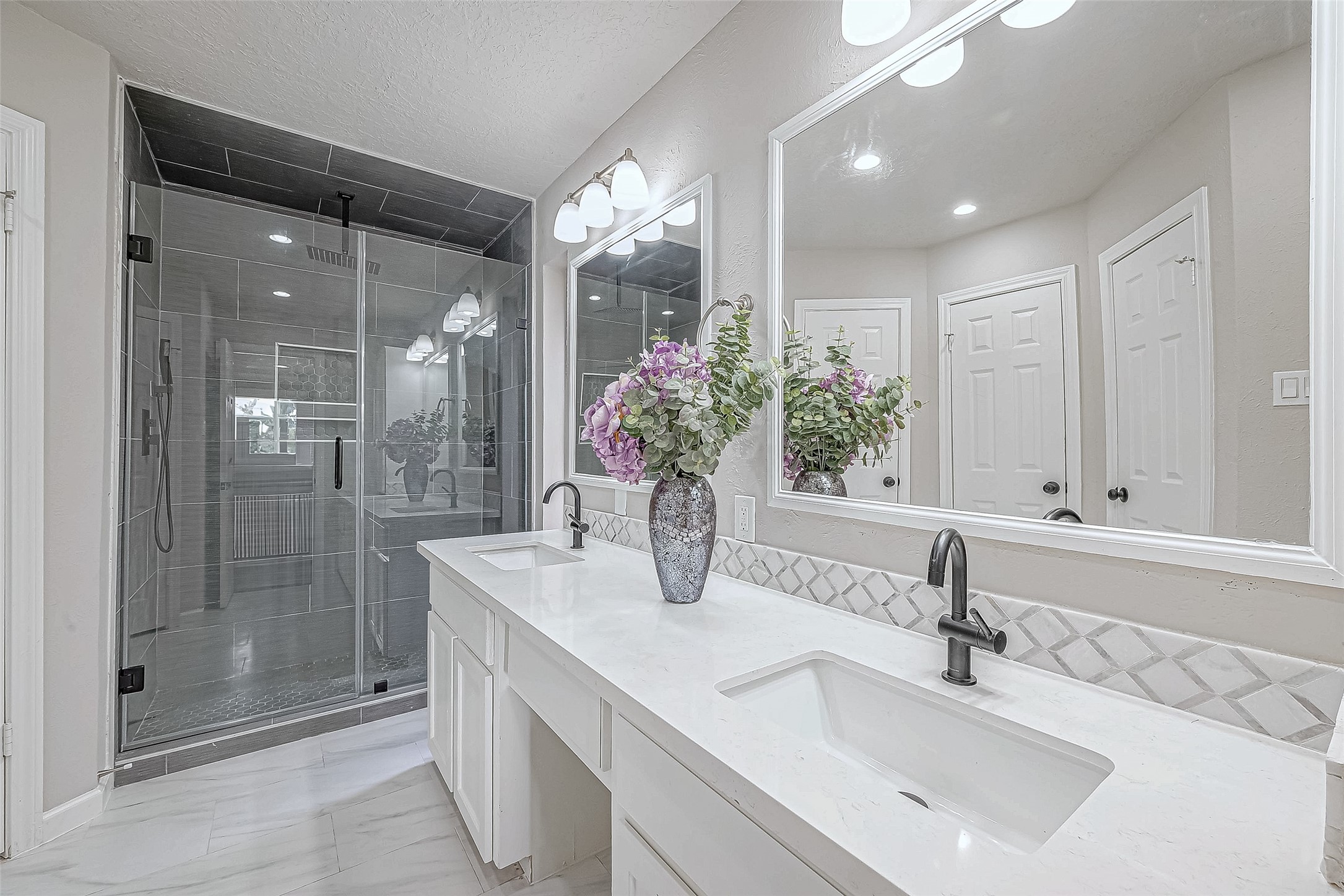 The primary bathroom with a spacious glass shower, dual sinks, sleek black fixtures, and large mirrors.