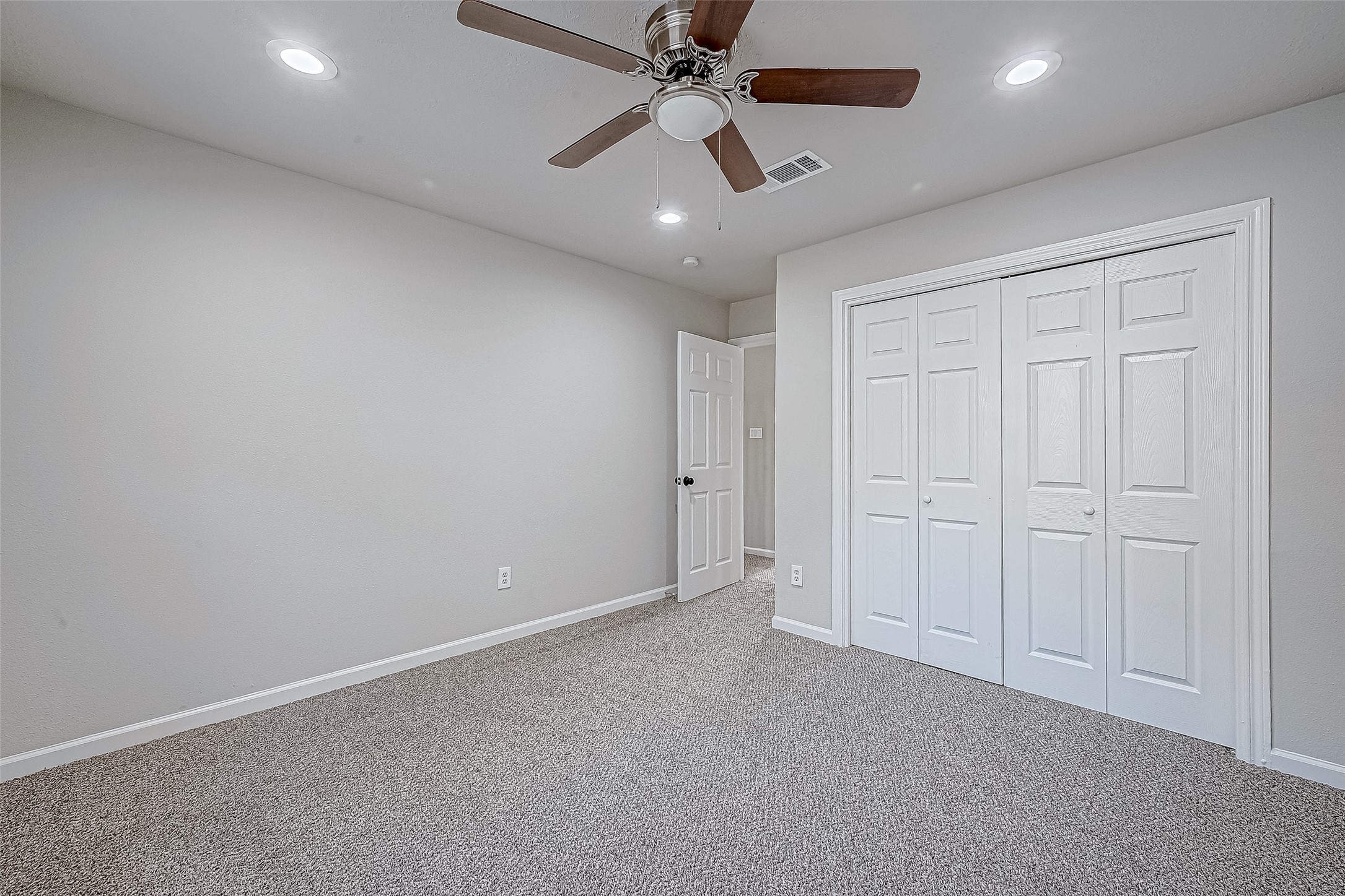 A carpeted bedroom with neutral walls, a ceiling fan, and a double-door closet for ample storage.
